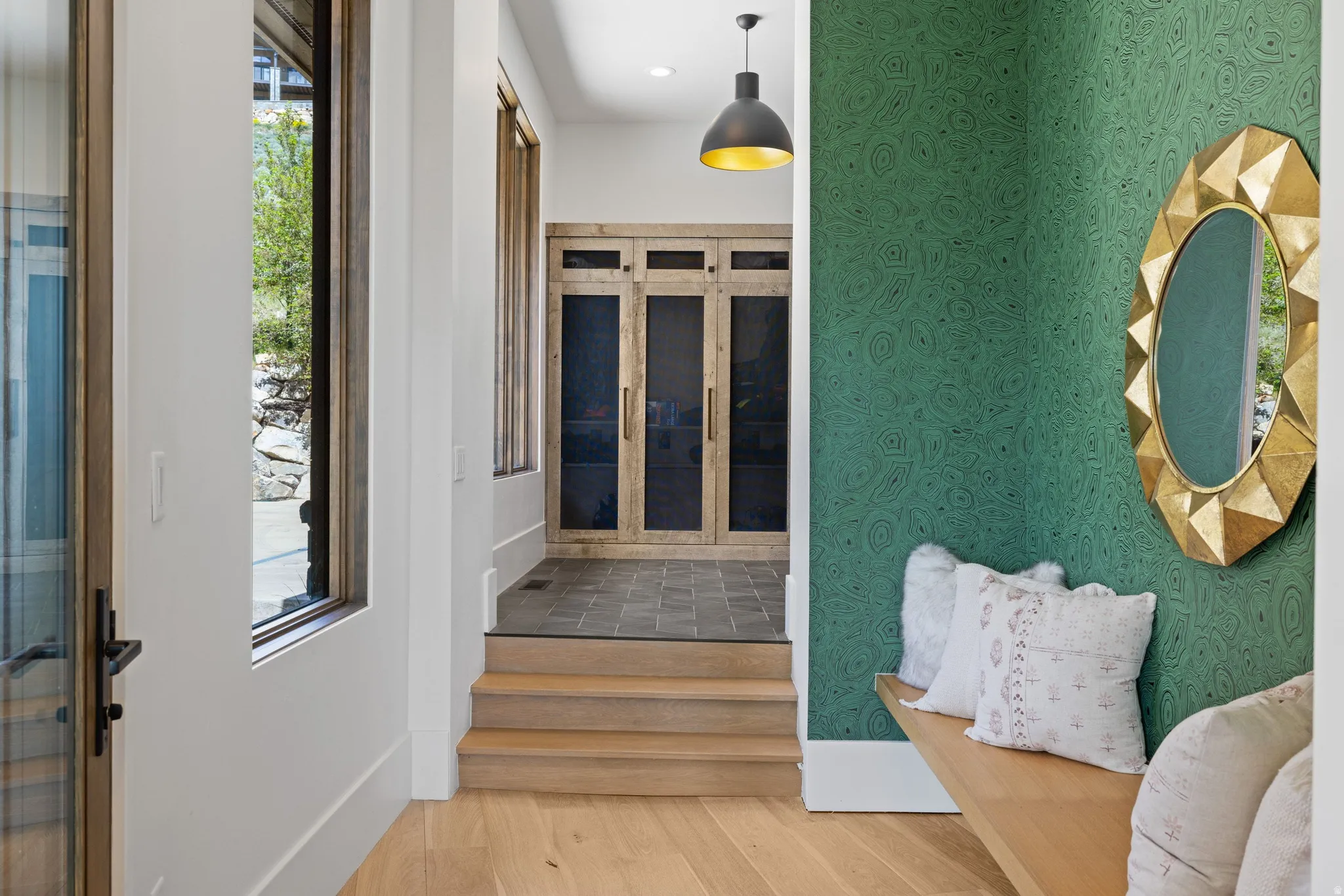 Foyer featuring wood-finish flooring, a wall with patterned green wallcovering, a built-in wood bench, and a gold-framed mirror