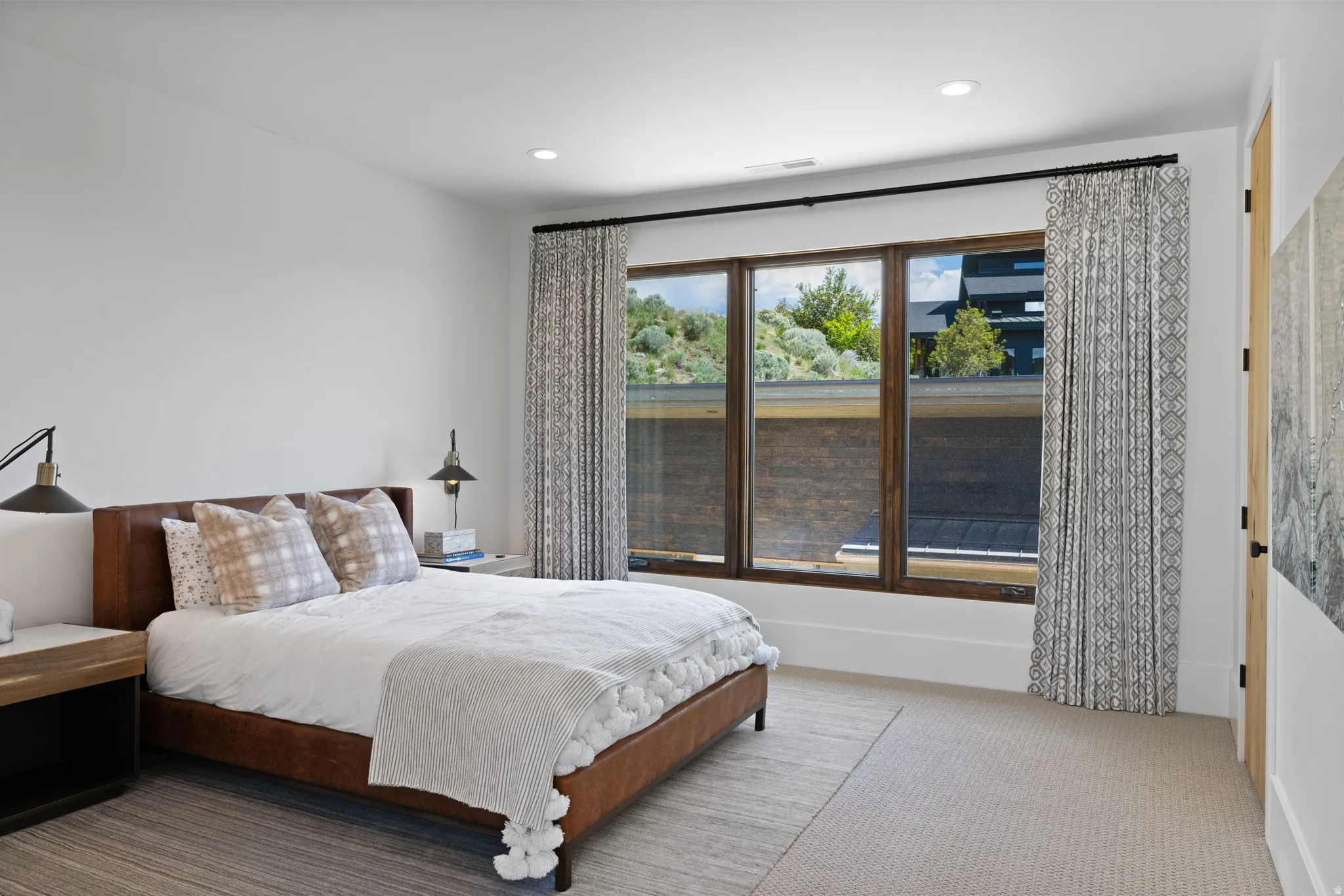 Bedroom featuring a multi-pane window with dark wood-finish framing, light neutral-toned carpeting, recessed ceiling lighting, a light wood-finish door, and white walls