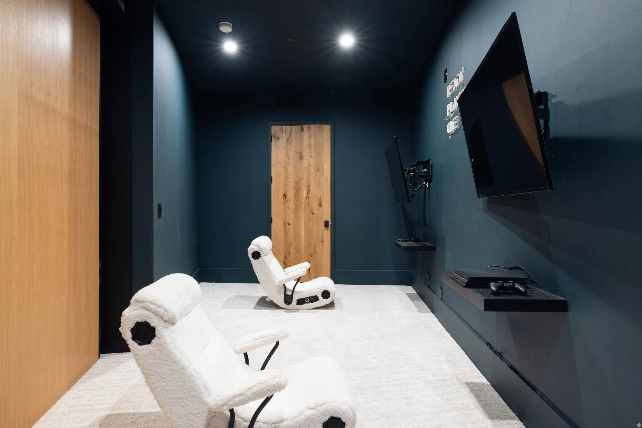 Dedicated media room featuring dark-painted walls, recessed ceiling lighting, a wood-finish door, wood-finish wall paneling, and wall-mounted shelving