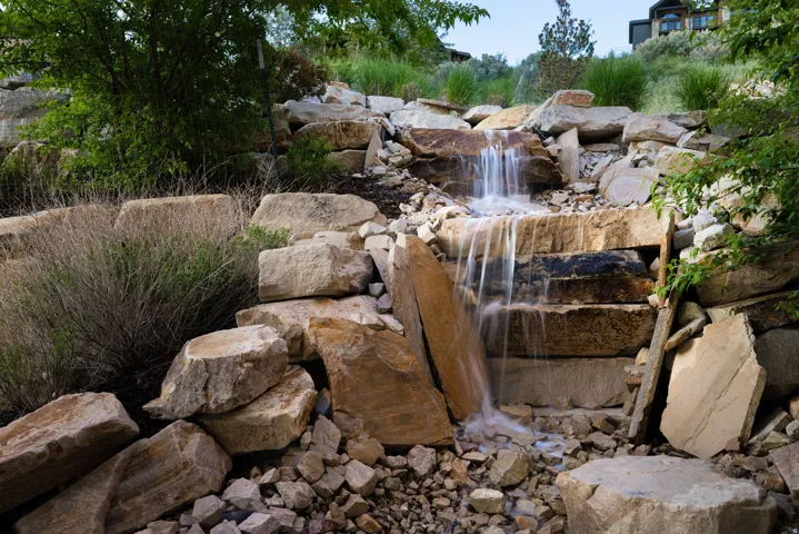 Tiered rock waterfall feature with natural stone landscaping, integrated into a sloped terrain
