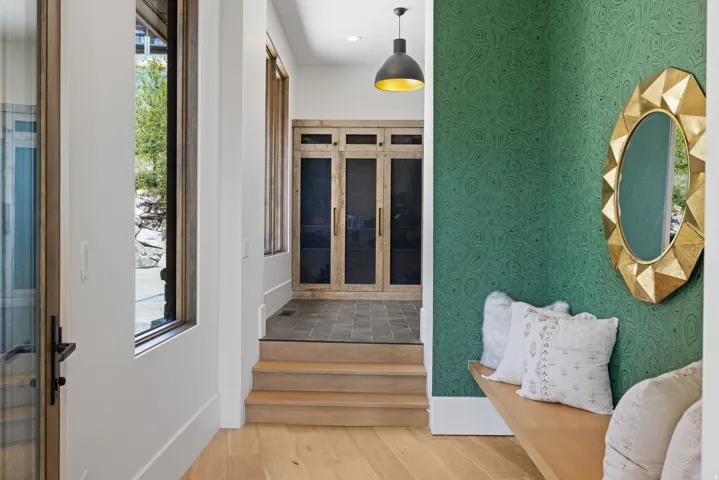Foyer featuring wood-finish flooring, a wall with patterned green wallcovering, a built-in wood bench, and a gold-framed mirror