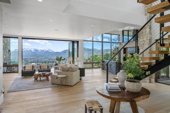 Spacious living area featuring large-format accordion glass doors, light wood-finish flooring, a stone-clad accent wall, open-tread stairs with a metal railing, and abundant natural light