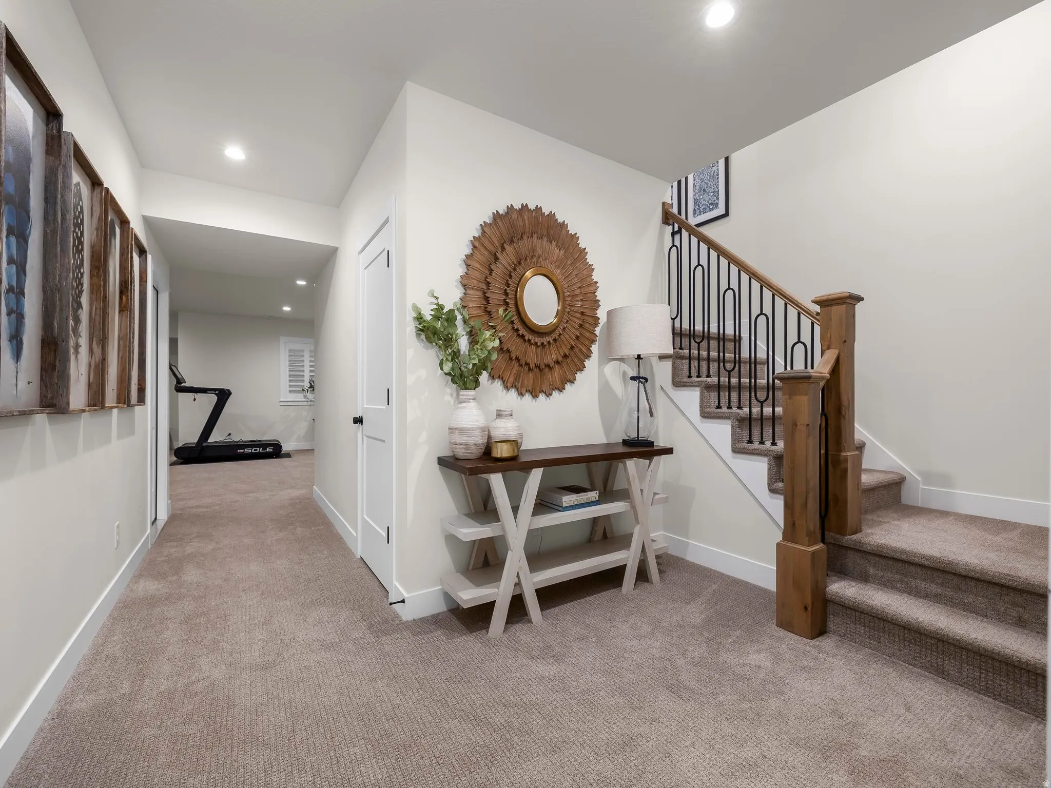 Carpeted hallway and staircase featuring a wood newel post and wrought iron balusters