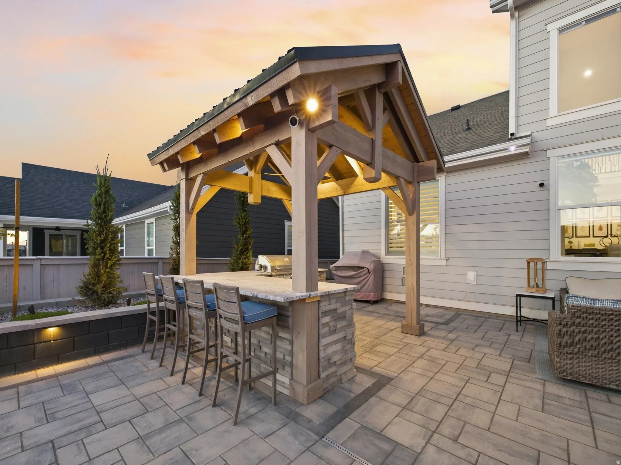 Outdoor kitchen under a wood-frame pavilion with built-in lighting