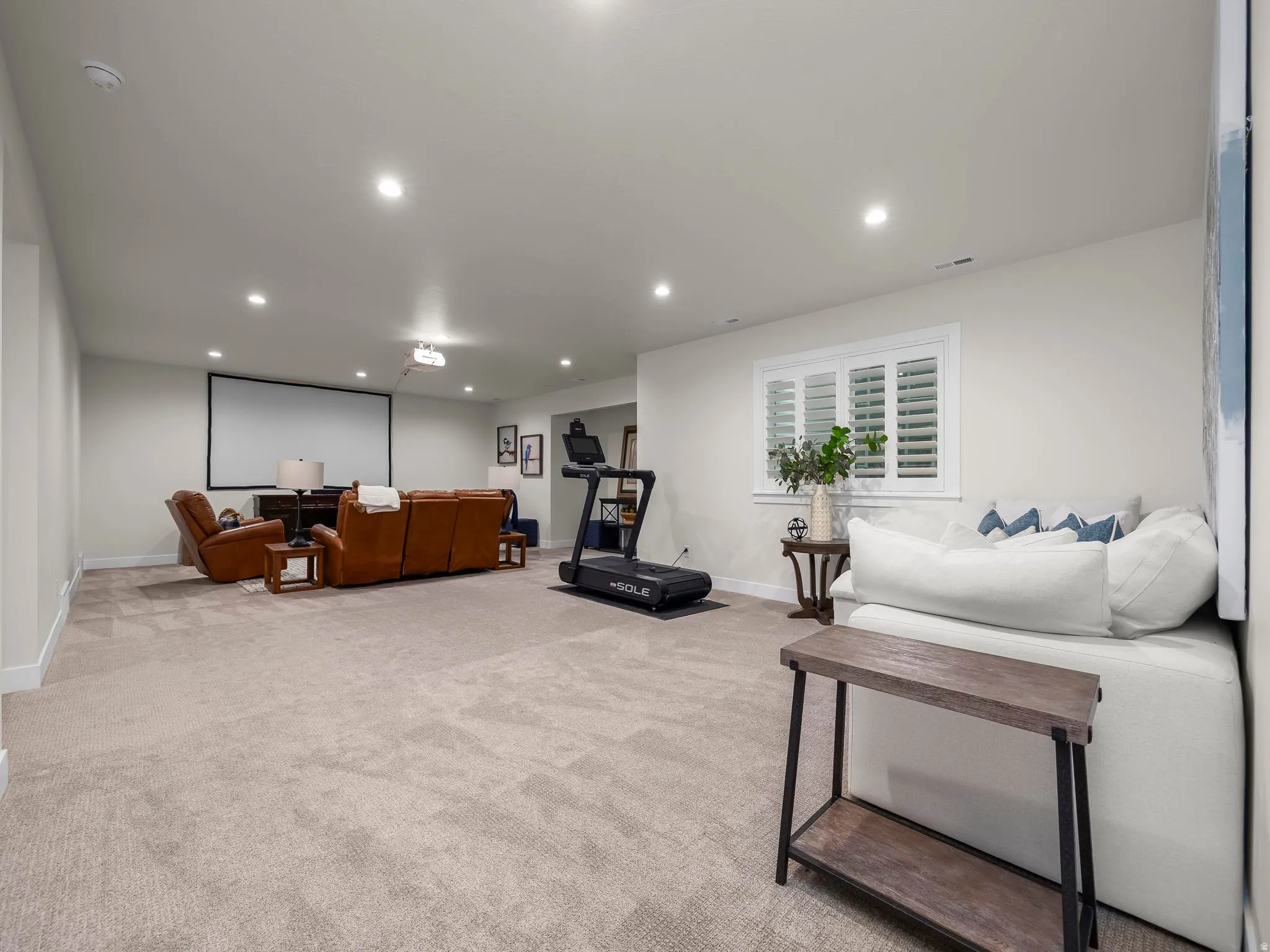 Expansive entertainment space featuring recessed lighting, a large projection screen, and a window with plantation shutters