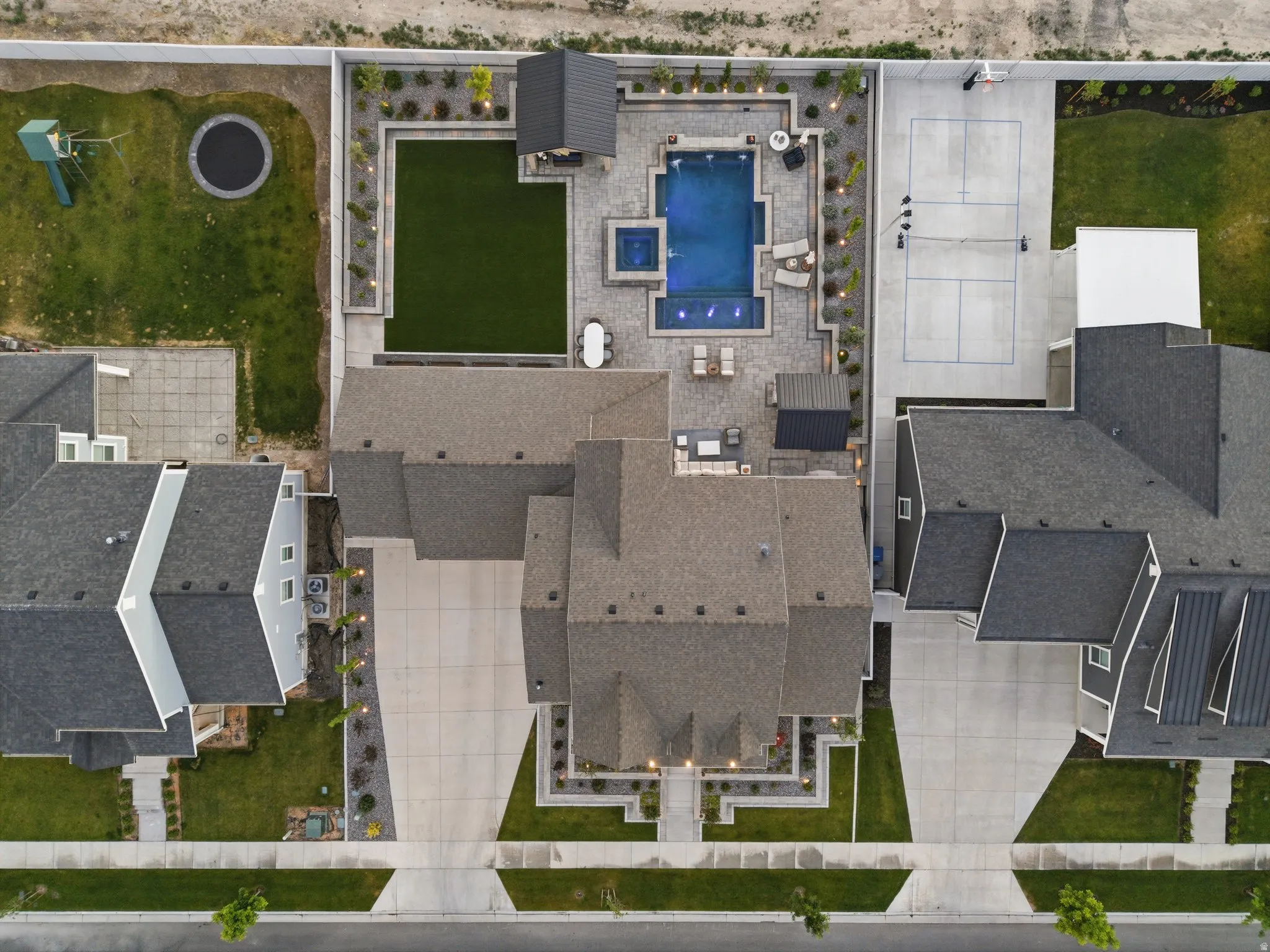 Expansive property featuring a large central residence, a dedicated sports court, a swimming pool with integrated spa, a separate artificial turf area, and extensive paver patio spaces
