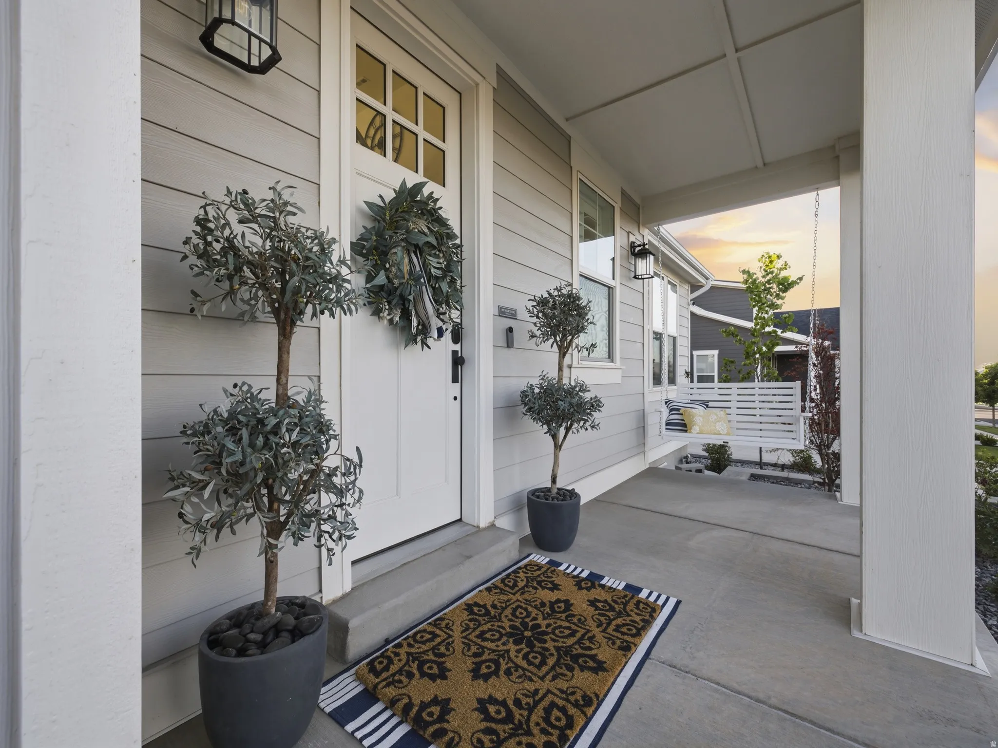 Covered front porch featuring light gray horizontal siding and a white front door with windowpanes