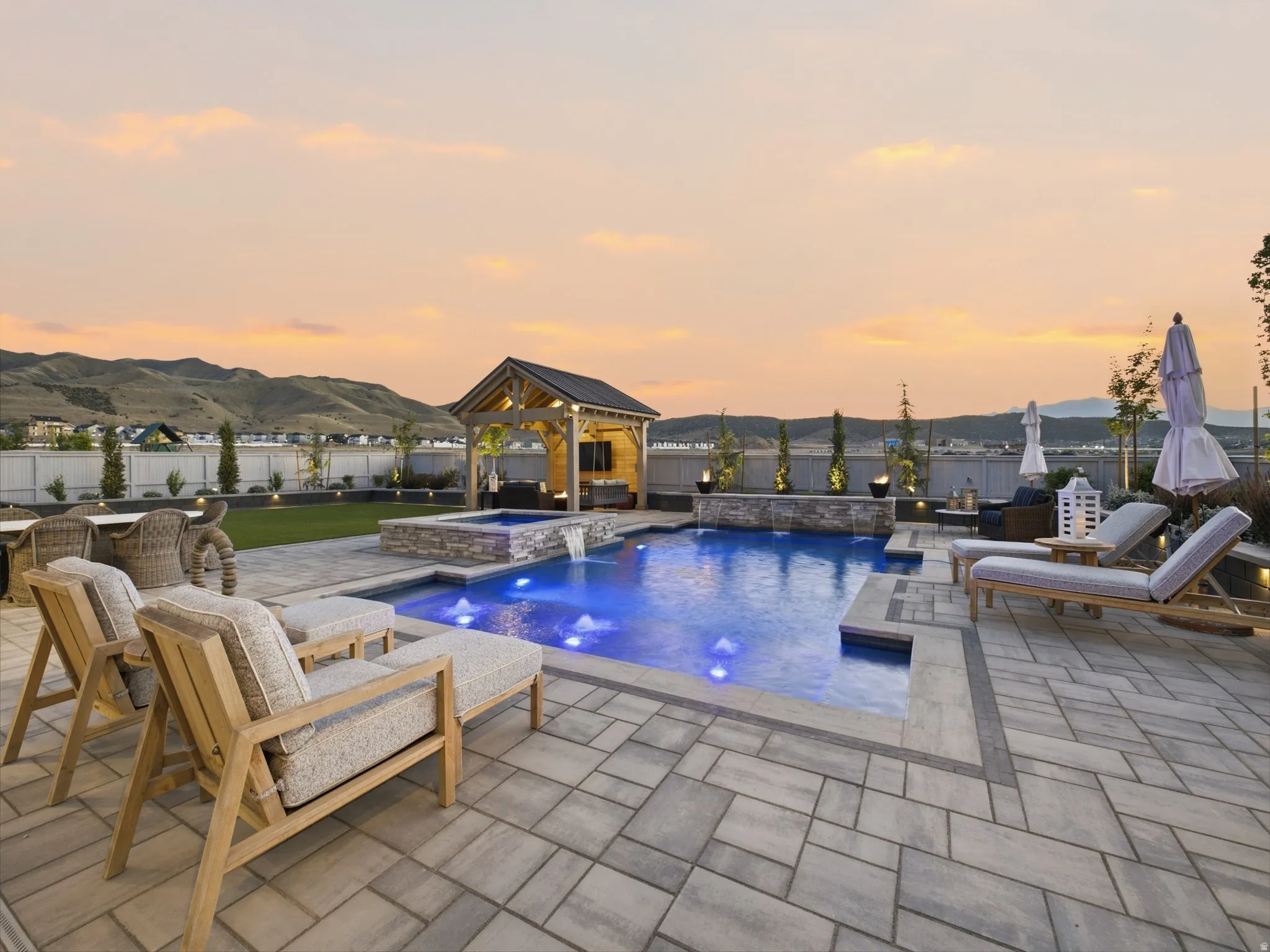 Expansive paver patio with a swimming pool, integrated spa with waterfall feature, and a covered outdoor structure