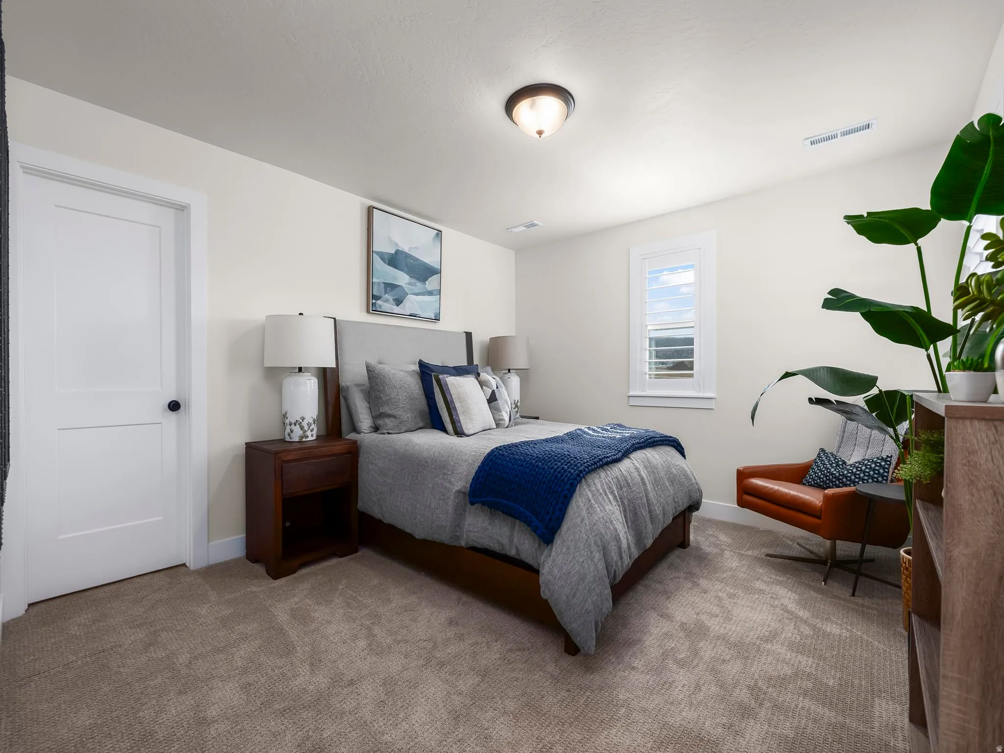 Bright bedroom with carpet flooring, a white paneled door, and a single window featuring horizontal blinds