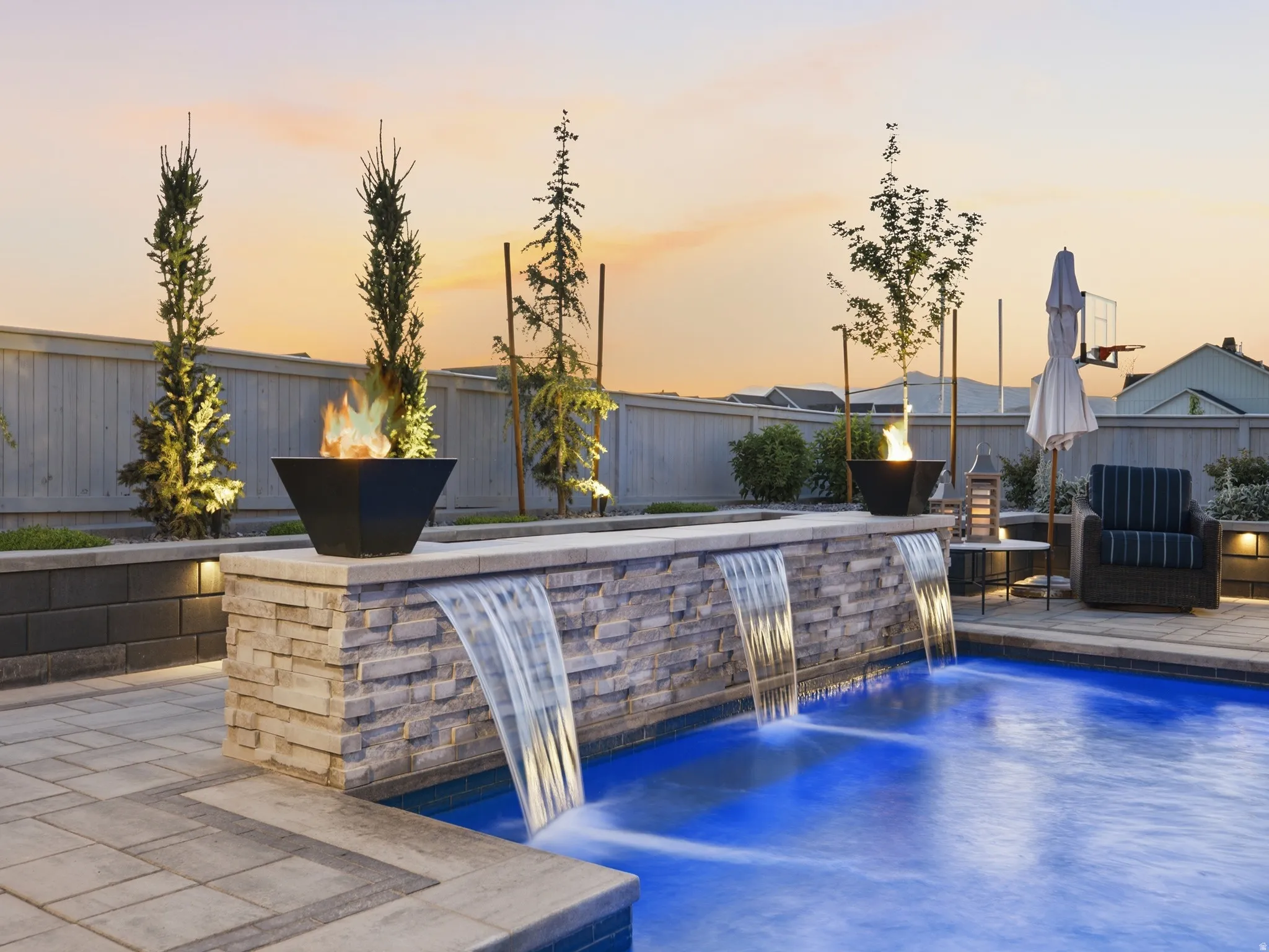 Swimming pool featuring three stone-clad waterfall descents and integrated fire bowls