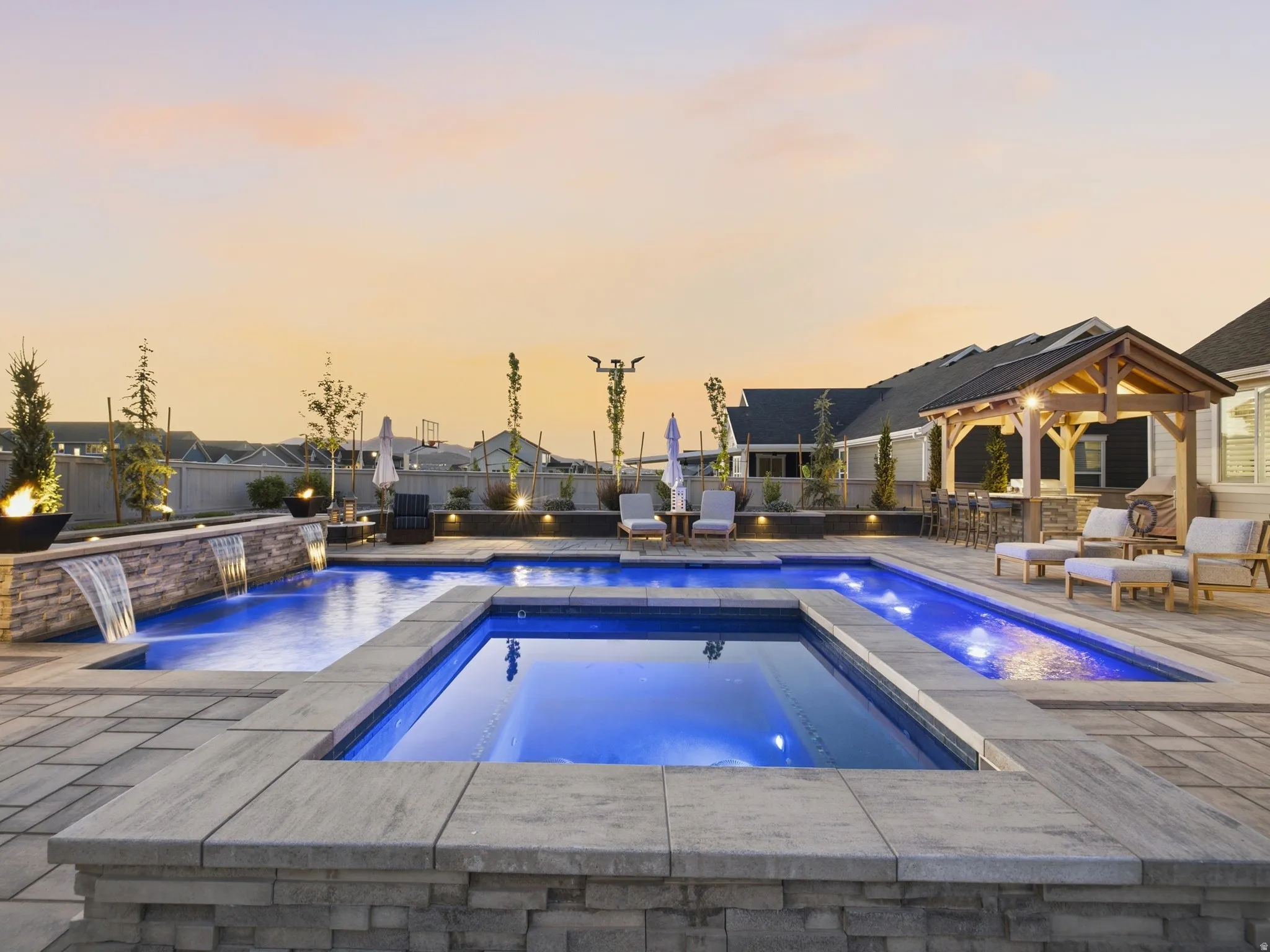 Expansive backyard featuring a multi-level pool with integrated spa, stone-clad water features, and an outdoor kitchen under a wood-frame gazebo