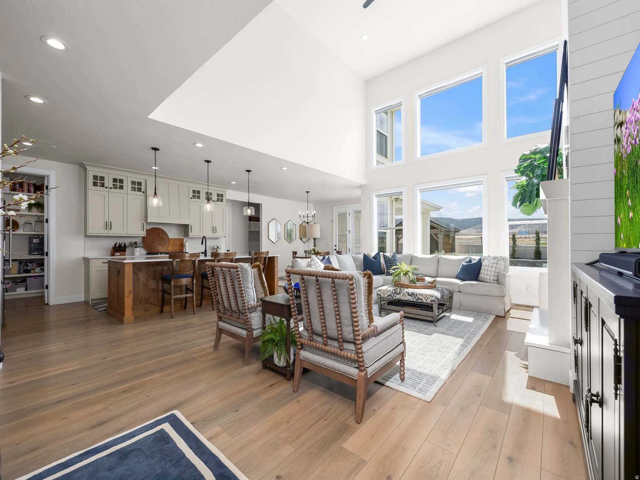 Open-concept living space featuring high ceilings, extensive window placement, light wood-finish flooring, a kitchen island with seating, and a walk-in pantry