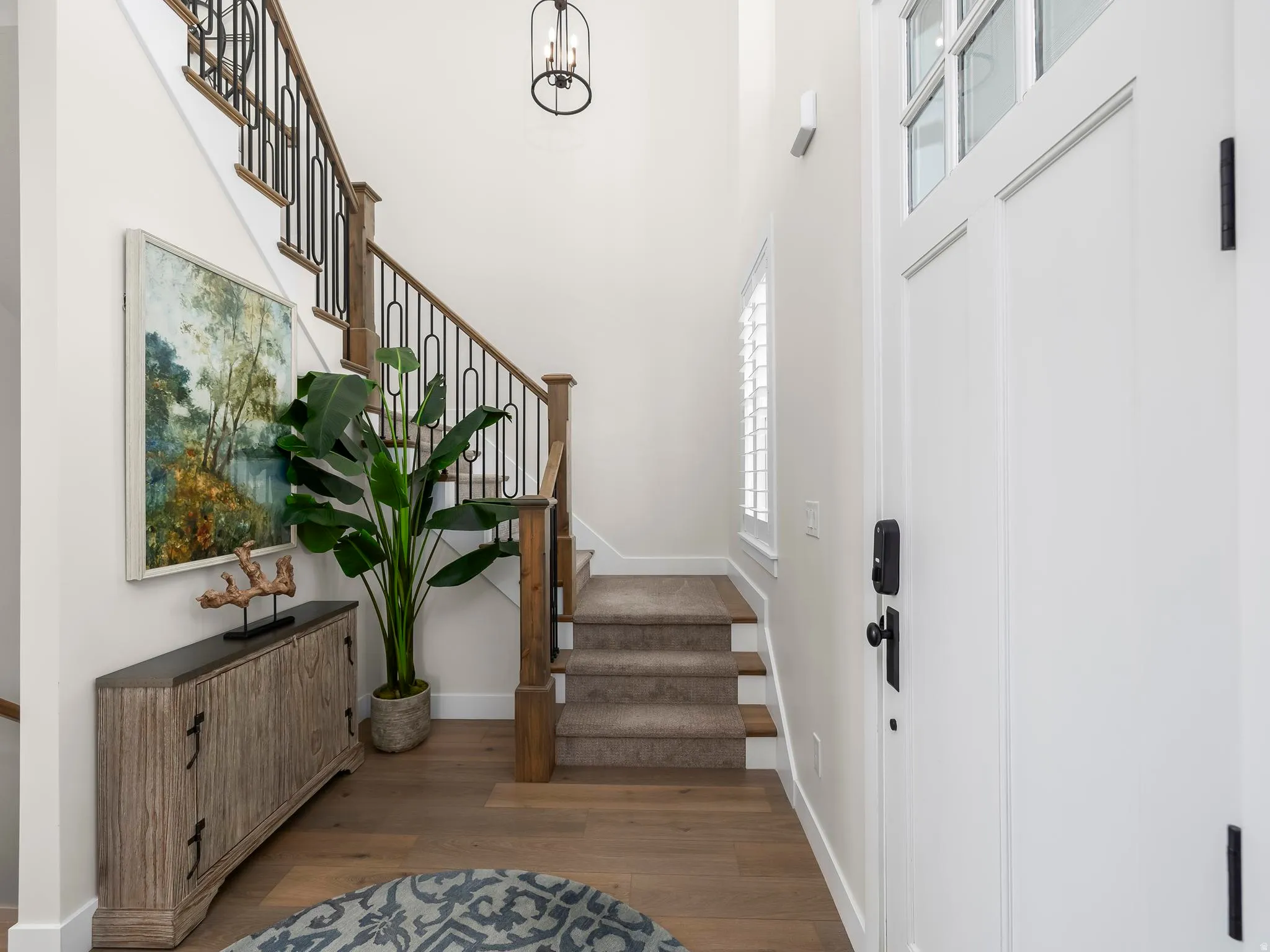 Entryway featuring wood-finish flooring, a two-story ceiling, and a staircase with wood newel posts and black metal balusters