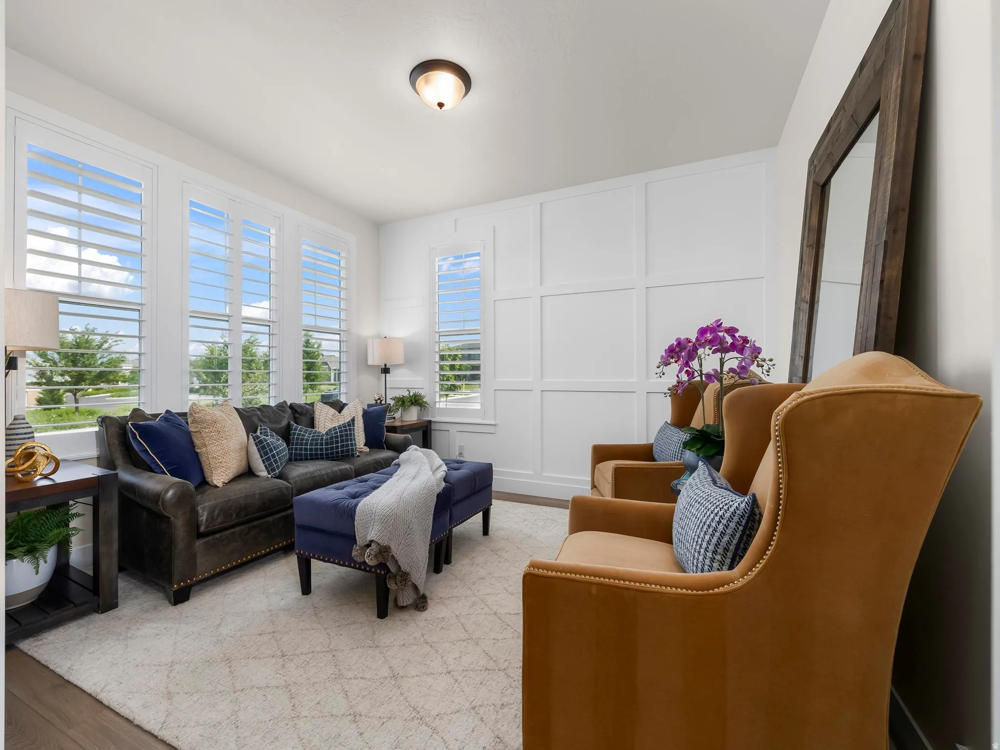 Living area featuring multiple windows with louvered shutters, a paneled accent wall, and wood-finish flooring