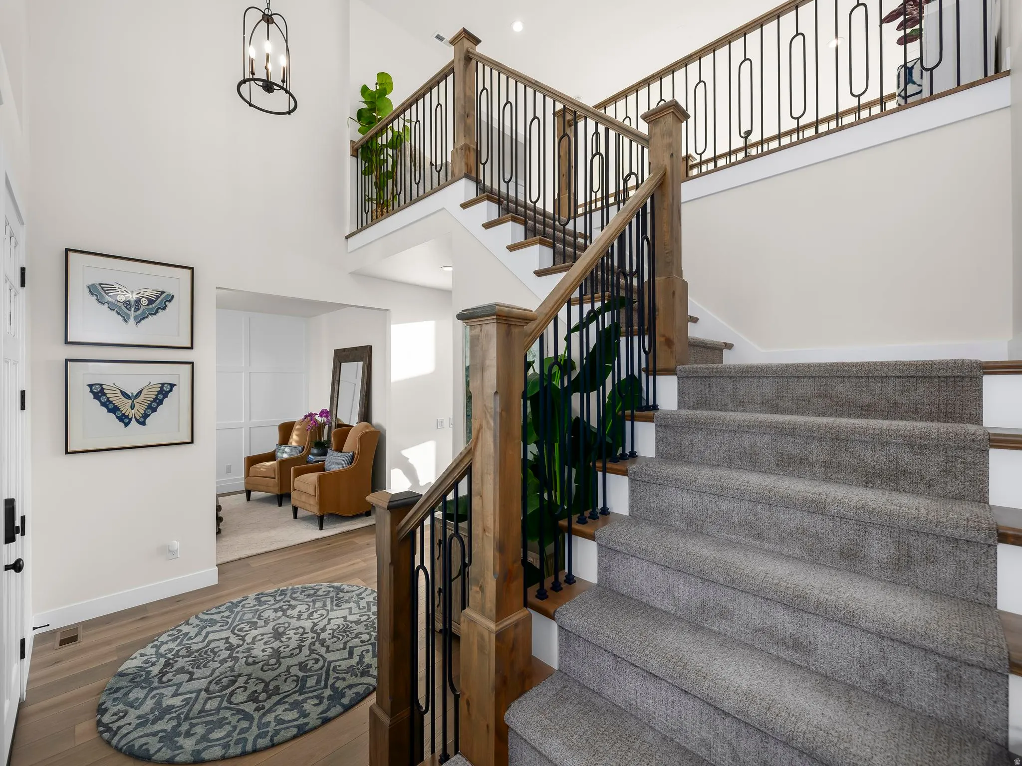 Two-story entry featuring wood-finish flooring, a carpeted staircase with a wood and wrought iron railing, and a vaulted ceiling with an iron chandelier