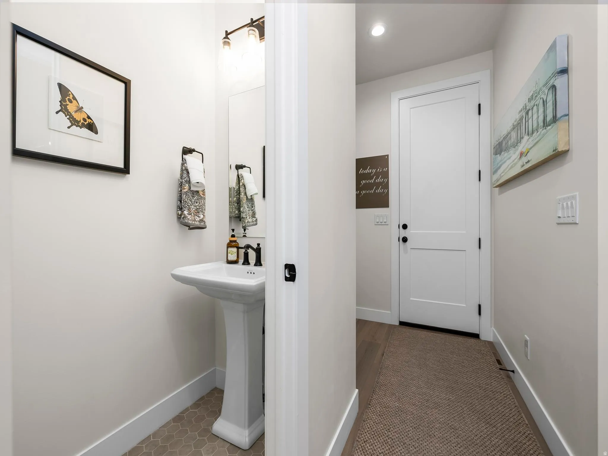 Pedestal sink with matte black faucet, hexagonal floor tiling, and a two-panel interior door with matte black hardware