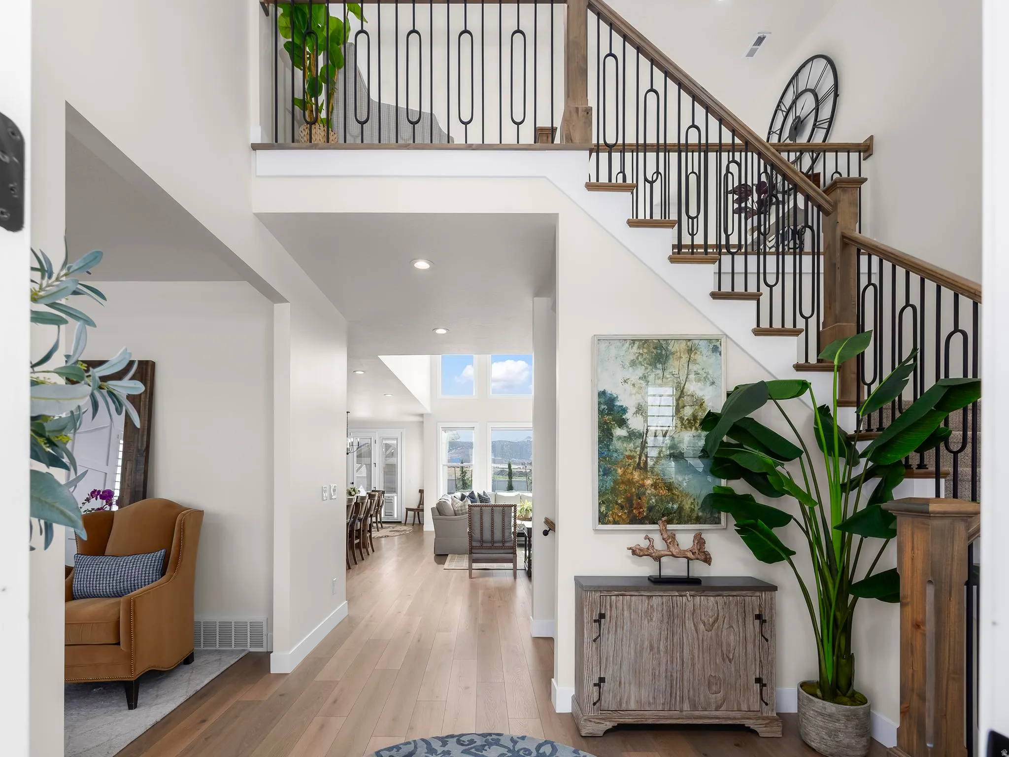 Two-story foyer featuring light wood-finish flooring, a grand staircase with dark metal balusters and wood handrails, and recessed lighting