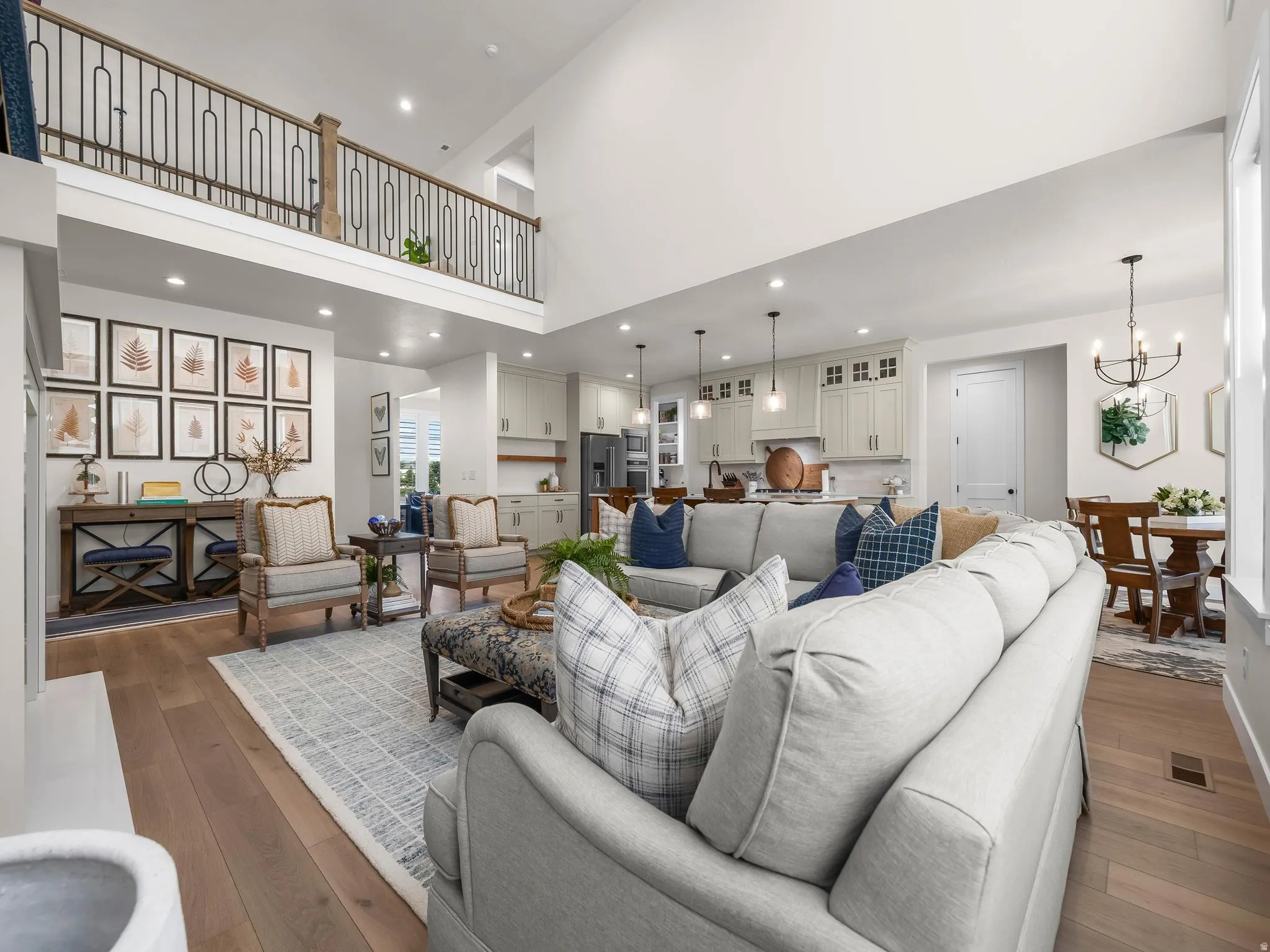 Spacious open-concept living area featuring high ceilings, wood-finish flooring, and a second-story interior balcony with an ornate metal railing