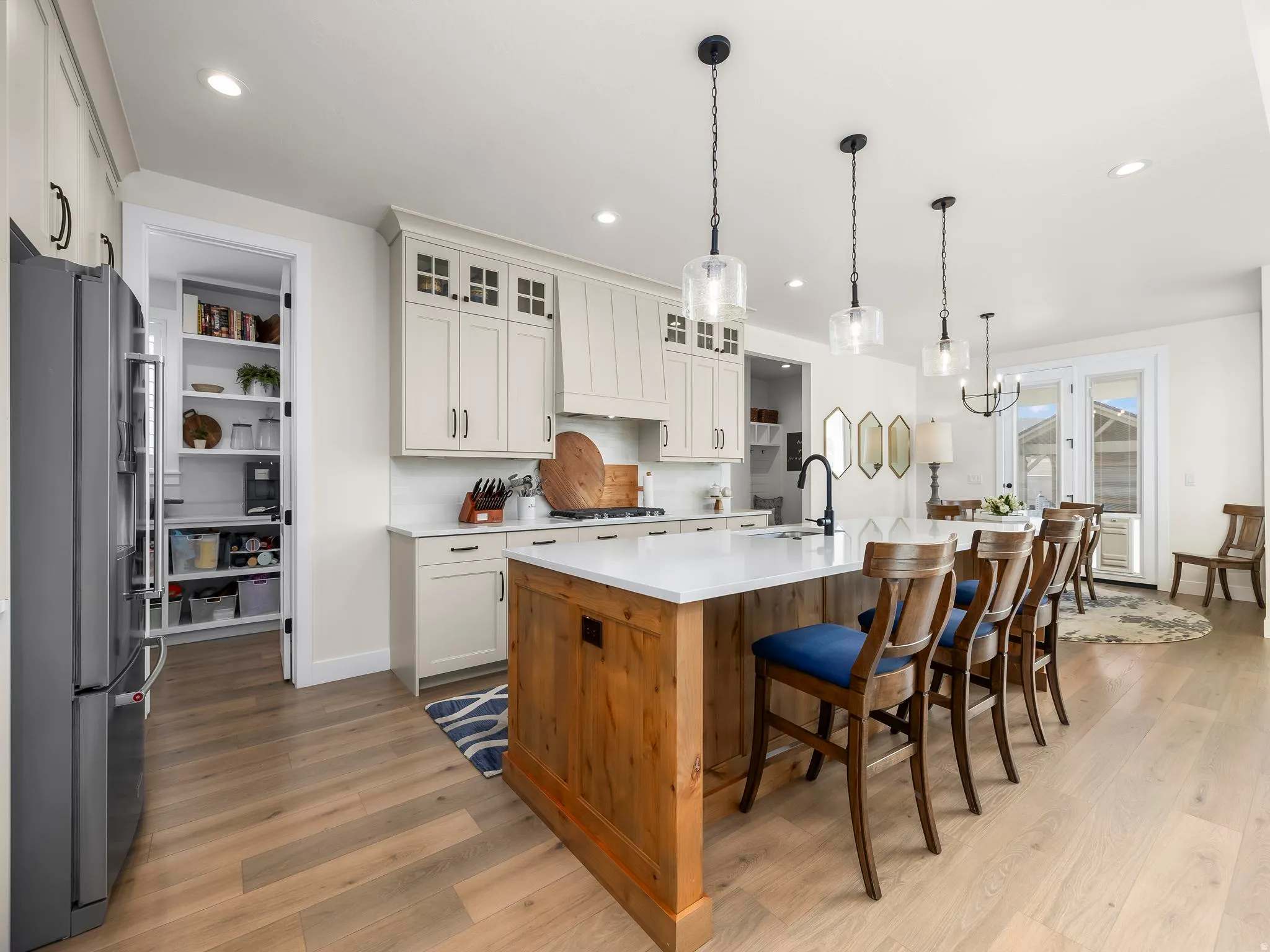 Spacious kitchen featuring a large island with white countertop, light wood-finish flooring, white cabinetry with dark hardware, and a walk-in pantry