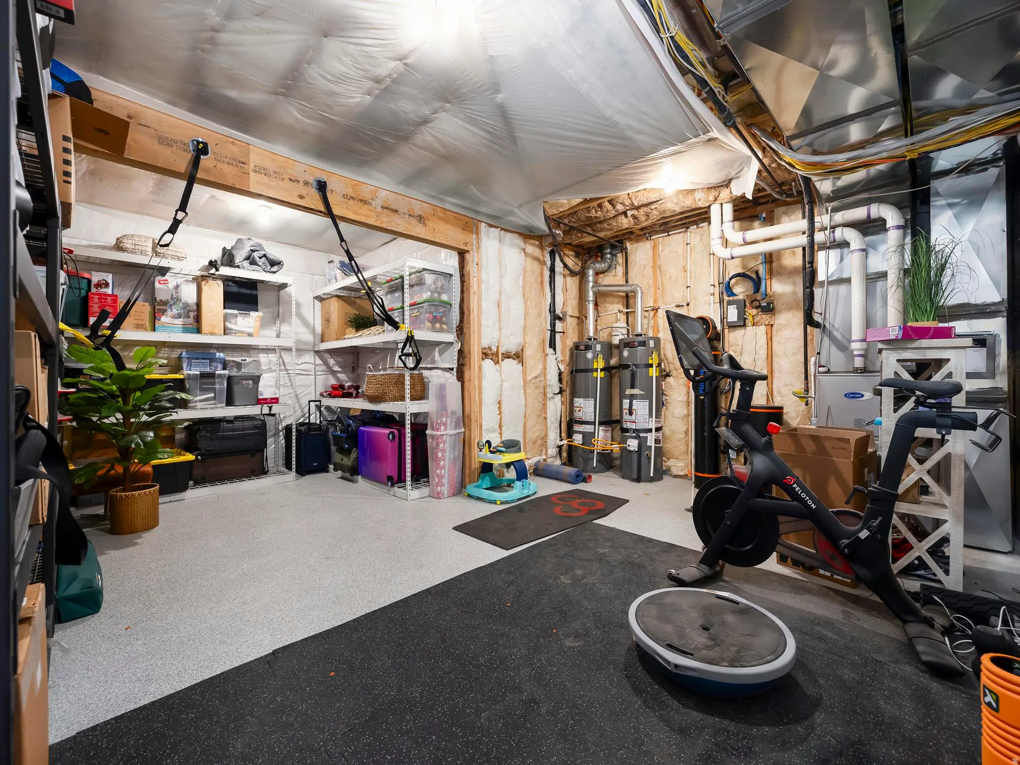 Utility space featuring a light-colored speckled flooring, exposed wooden beams, and multiple water heaters