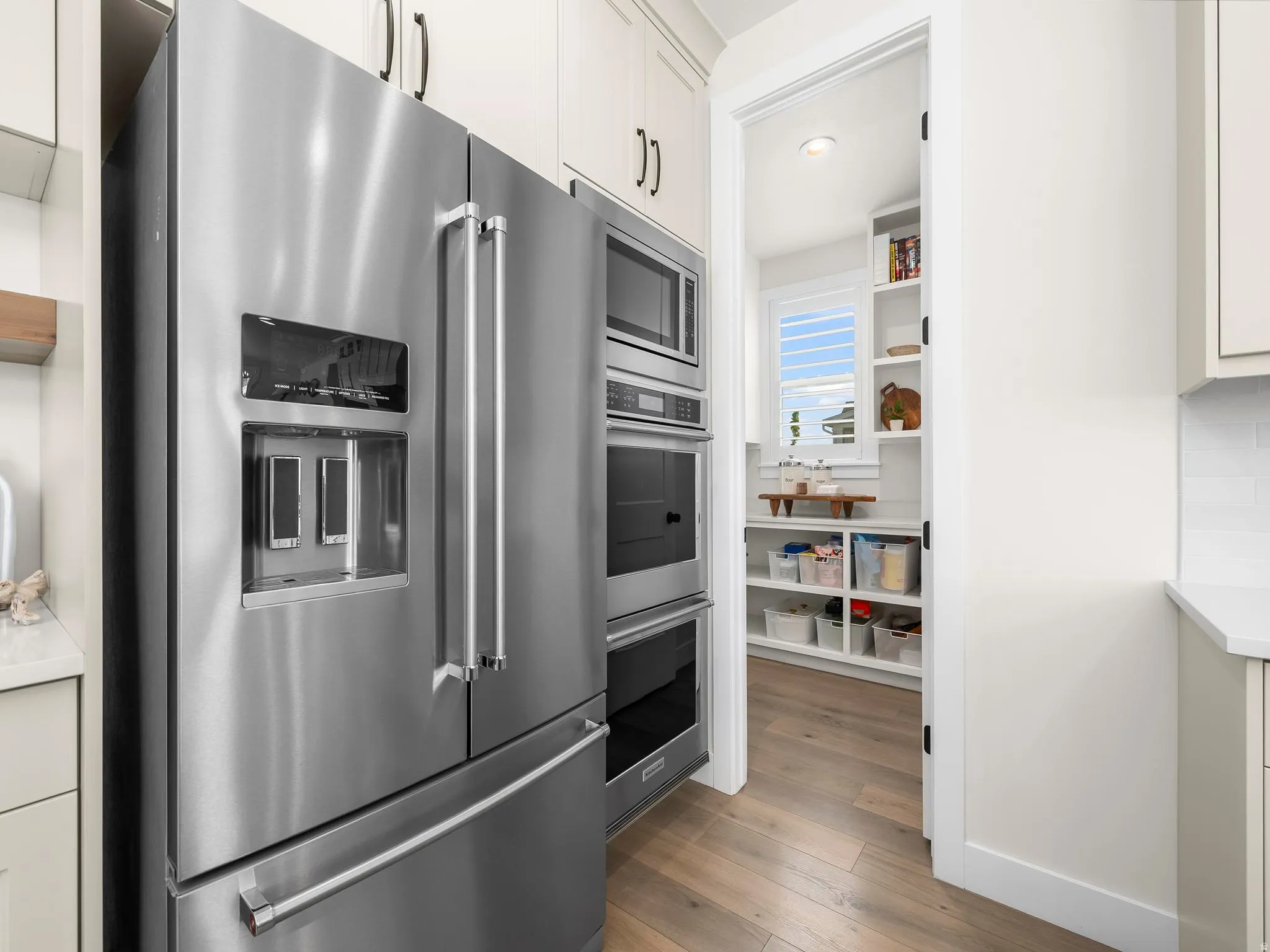 Stainless steel French door refrigerator with integrated ice and water dispenser, accompanied by built-in wall oven and microwave