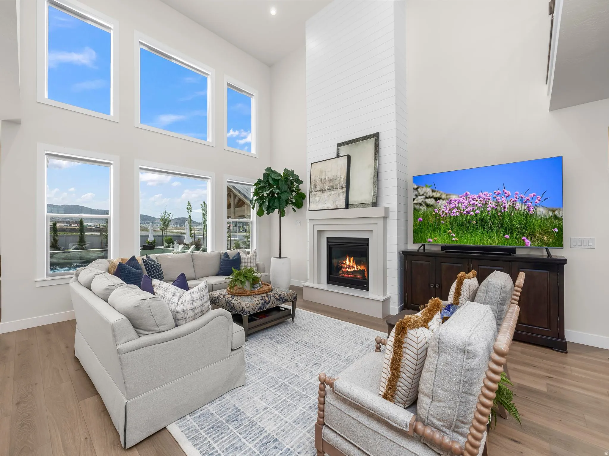 Living area featuring a floor-to-ceiling fireplace with a shiplap surround and mantel, wood-finish flooring, and a bank of high-set windows