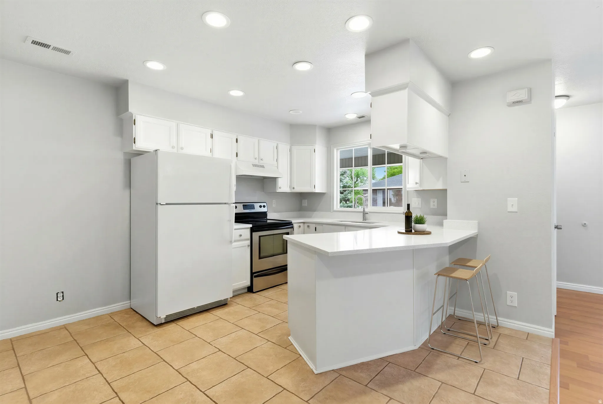 Kitchen featuring white cabinetry, stainless steel range, ceramic tile flooring, recessed lighting, and a breakfast bar