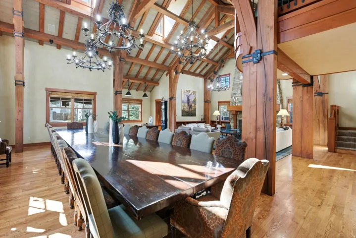 Expansive dining area featuring a vaulted wood-beam ceiling, multiple decorative chandeliers, skylights, and wood-finish flooring