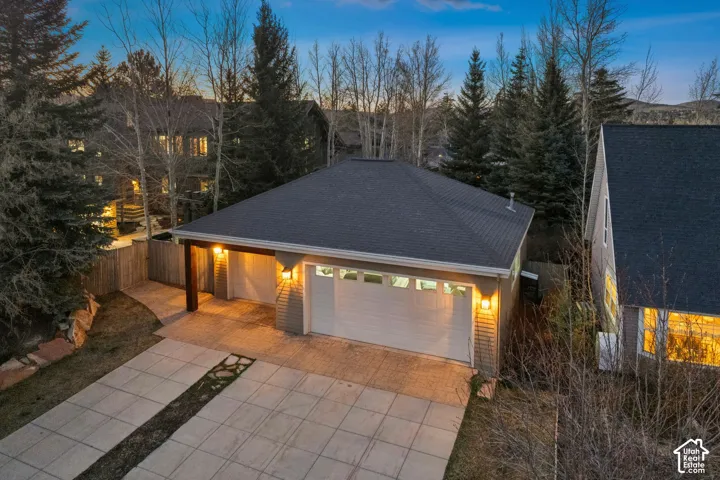 Two-car garage with overhead lighting, covered carport, and a paved driveway featuring decorative stone elements