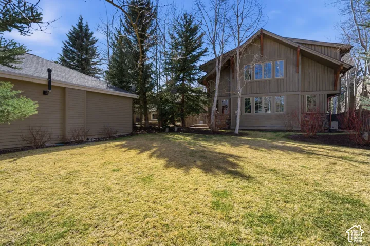 Expansive lawn area with mature evergreen trees, complemented by a multi-story residence featuring extensive window placements and exposed architectural elements
