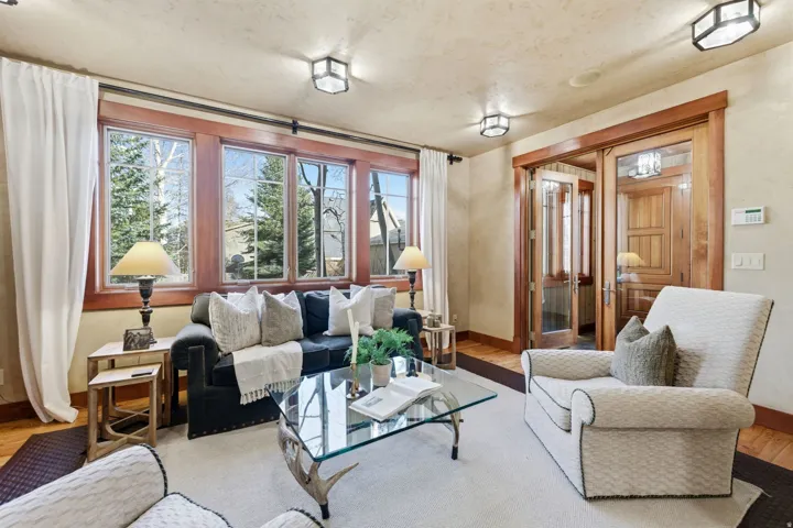 Living area featuring a wall of multi-pane windows with wood trim, hardwood flooring, and a pair of glass-paned French doors with wood framing