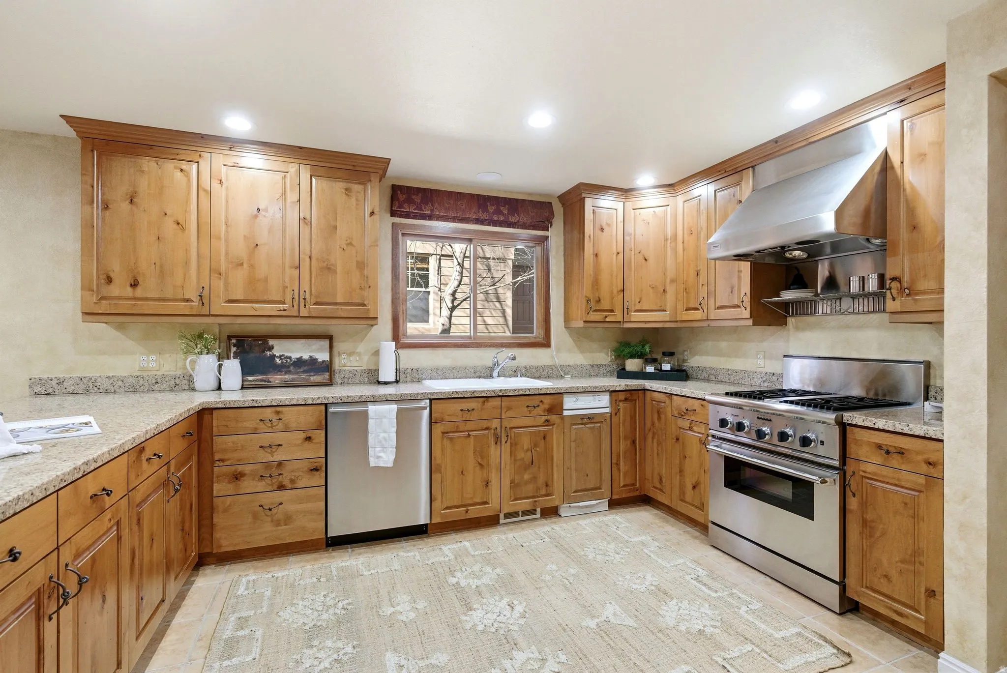 Spacious kitchen featuring natural wood cabinetry, light-toned countertops, a stainless steel range with a matching range hood, a stainless steel dishwasher, and recessed lighting