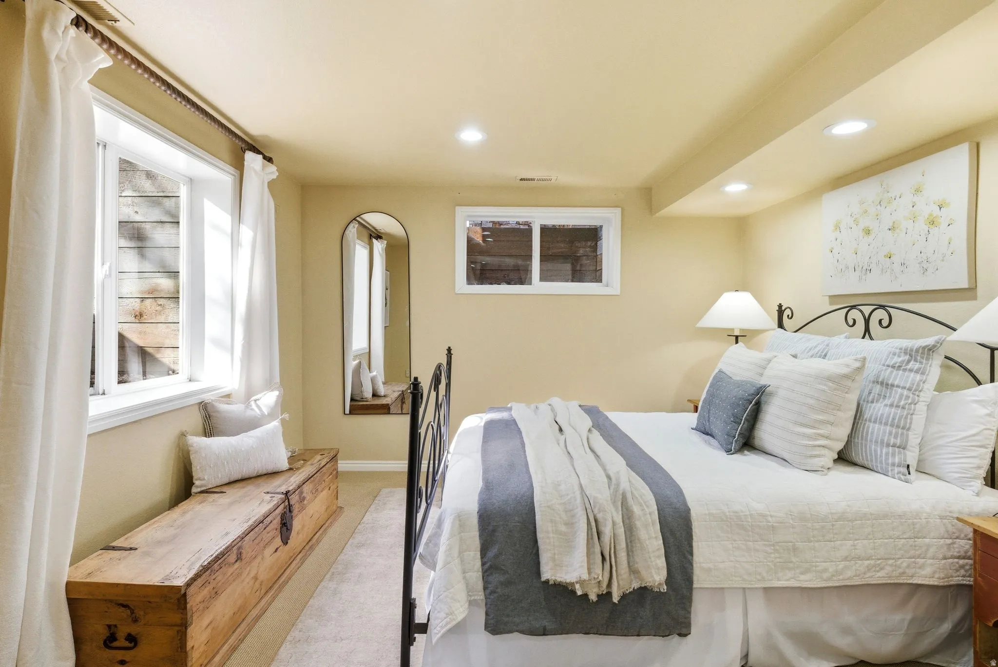 Recessed lighting illuminates this room, featuring a large window with white curtains and a smaller egress window