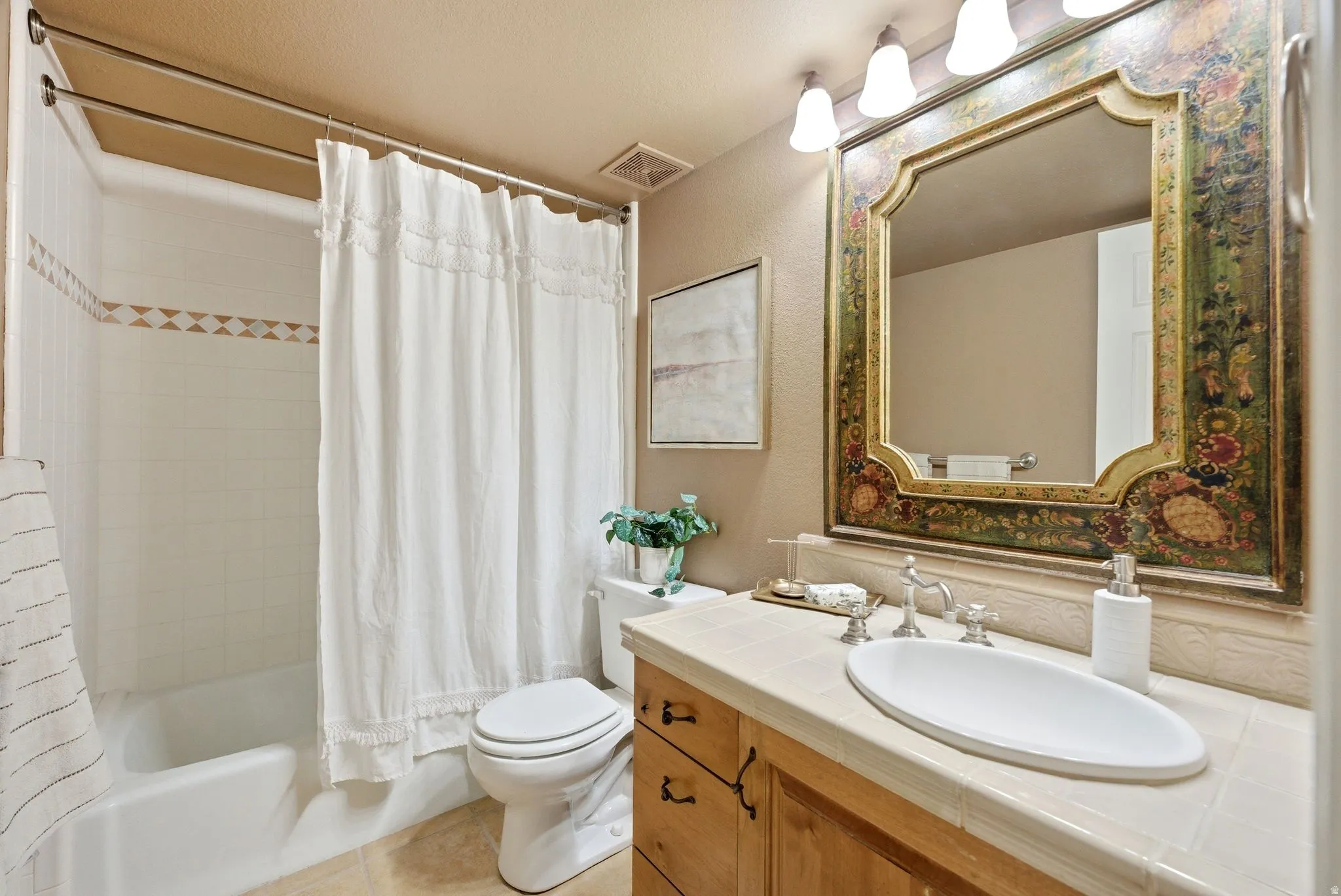 Full bathroom featuring a tub-shower combination with white tile surround and decorative accent tile, a single vanity with wood cabinetry, a tile countertop, and a decorative framed mirror