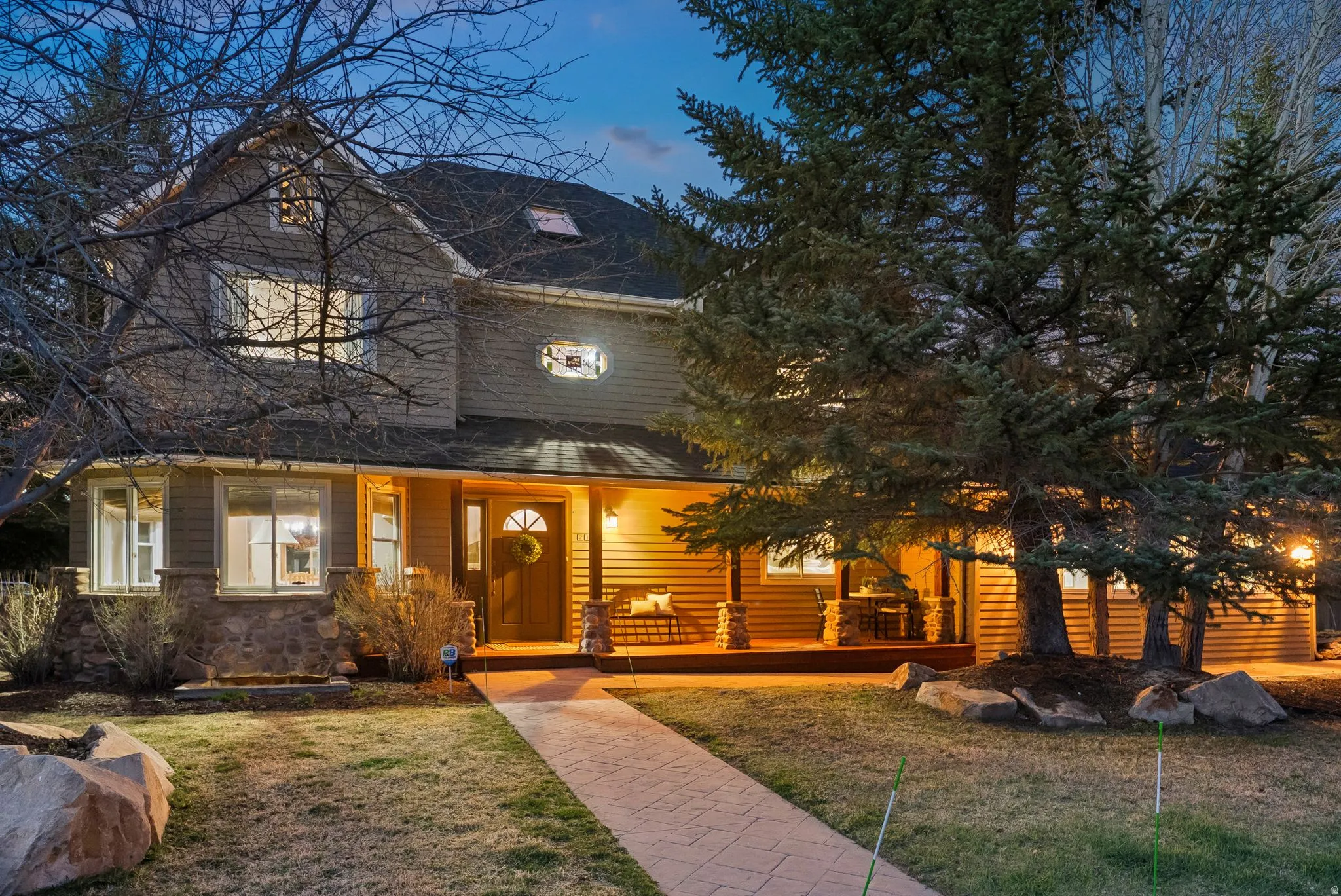 Two-story residence featuring a covered front porch, stone accents, shingle siding, and a paved walkway