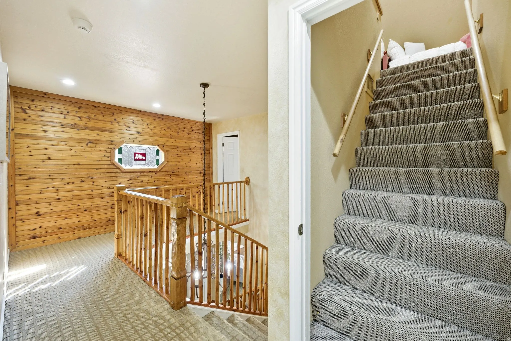 Upper-level landing featuring a wood-paneled accent wall with an octagonal stained-glass window, recessed lighting, and a chandelier