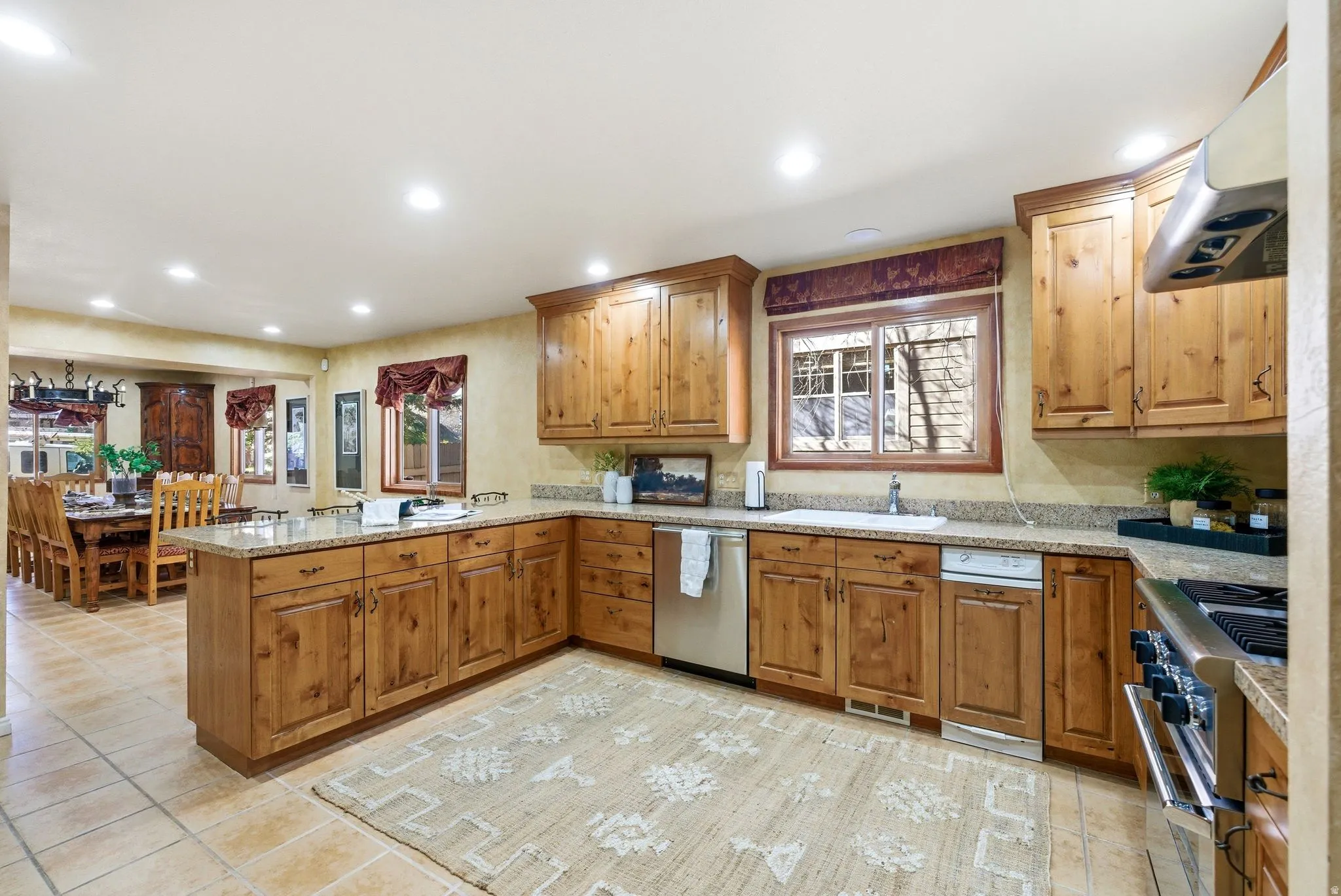 Spacious kitchen featuring extensive wood cabinetry, stone countertops, stainless steel appliances, and tile flooring