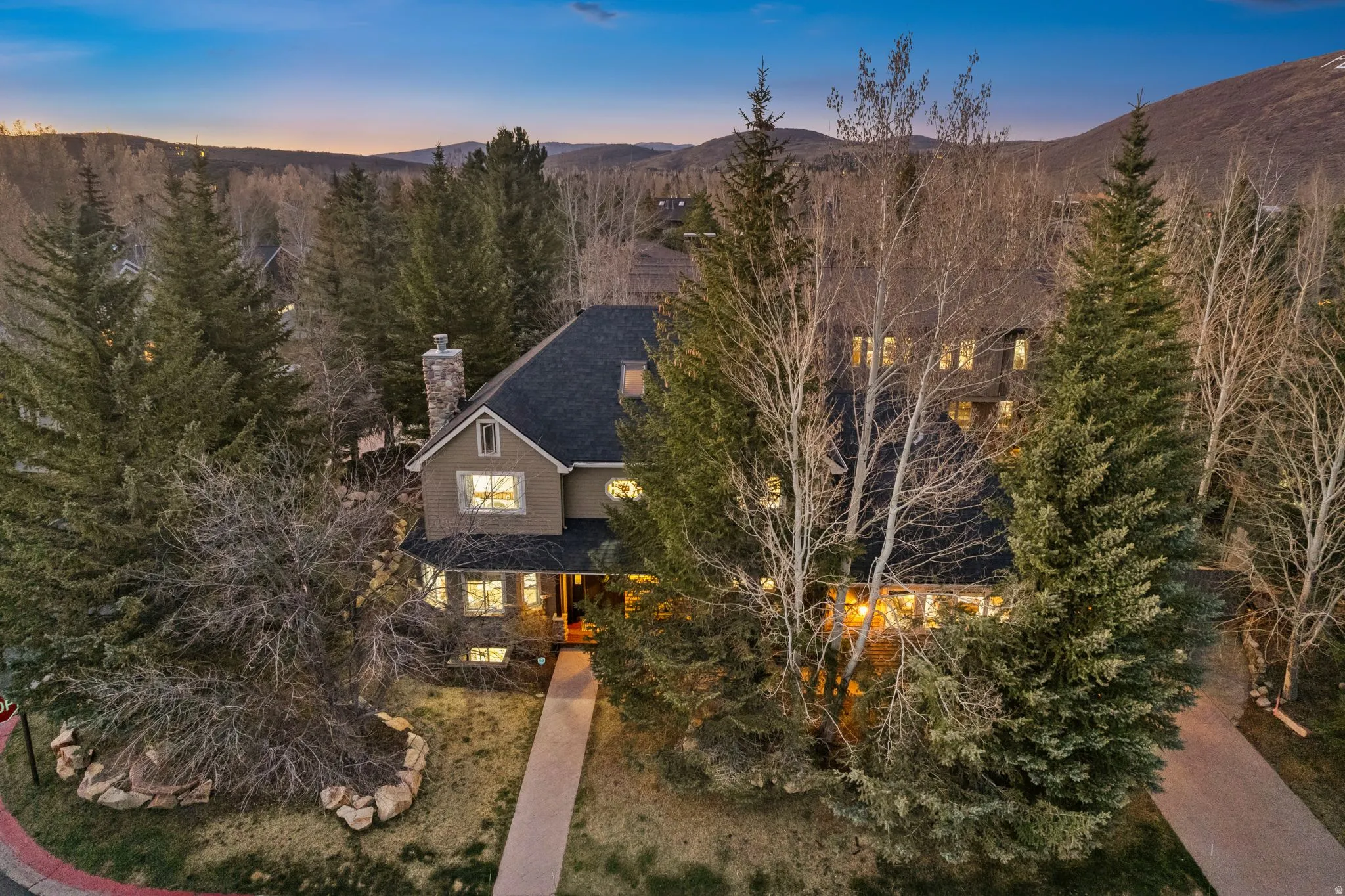 Multistory residence featuring a prominent stone chimney, dark shingle roof, and light-colored stucco siding