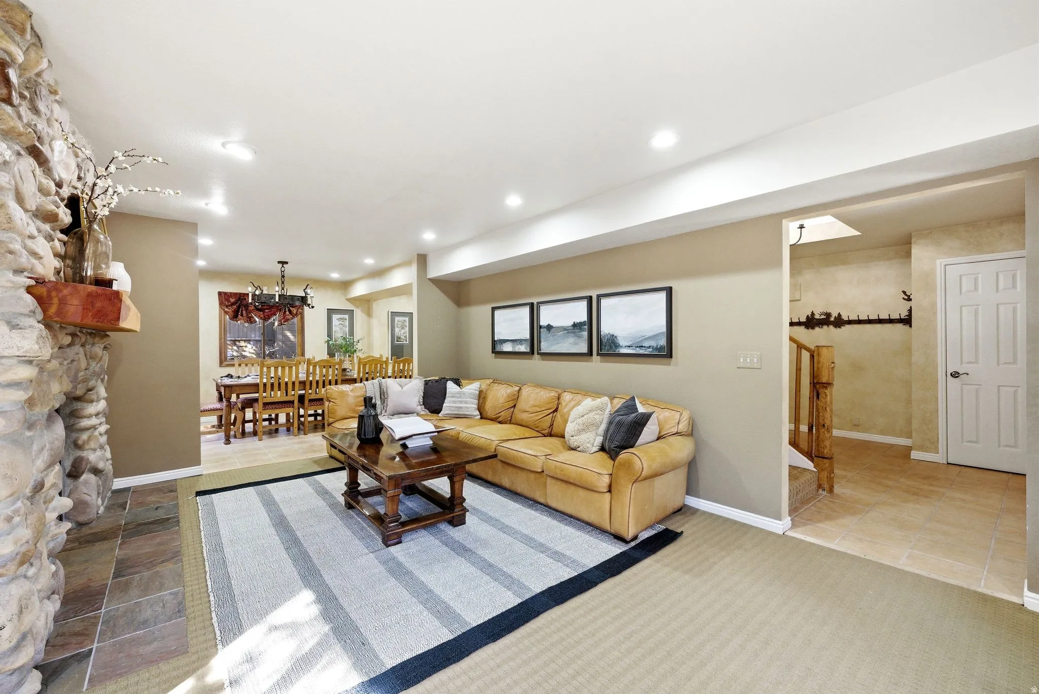Living area featuring a stone-clad fireplace with a wood mantle, recessed lighting, and a dining area visible beyond