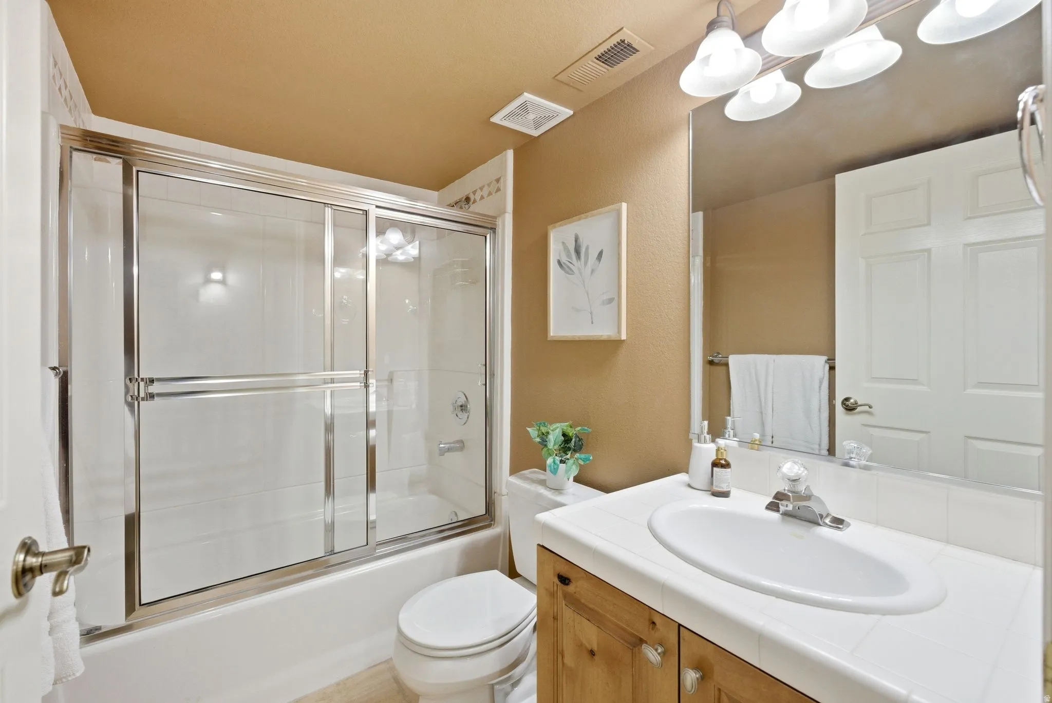 Full bathroom featuring a white tub and shower combination with sliding glass doors, a single vanity with wood-finish cabinetry, an integrated white sink, and a large wall-mounted mirror