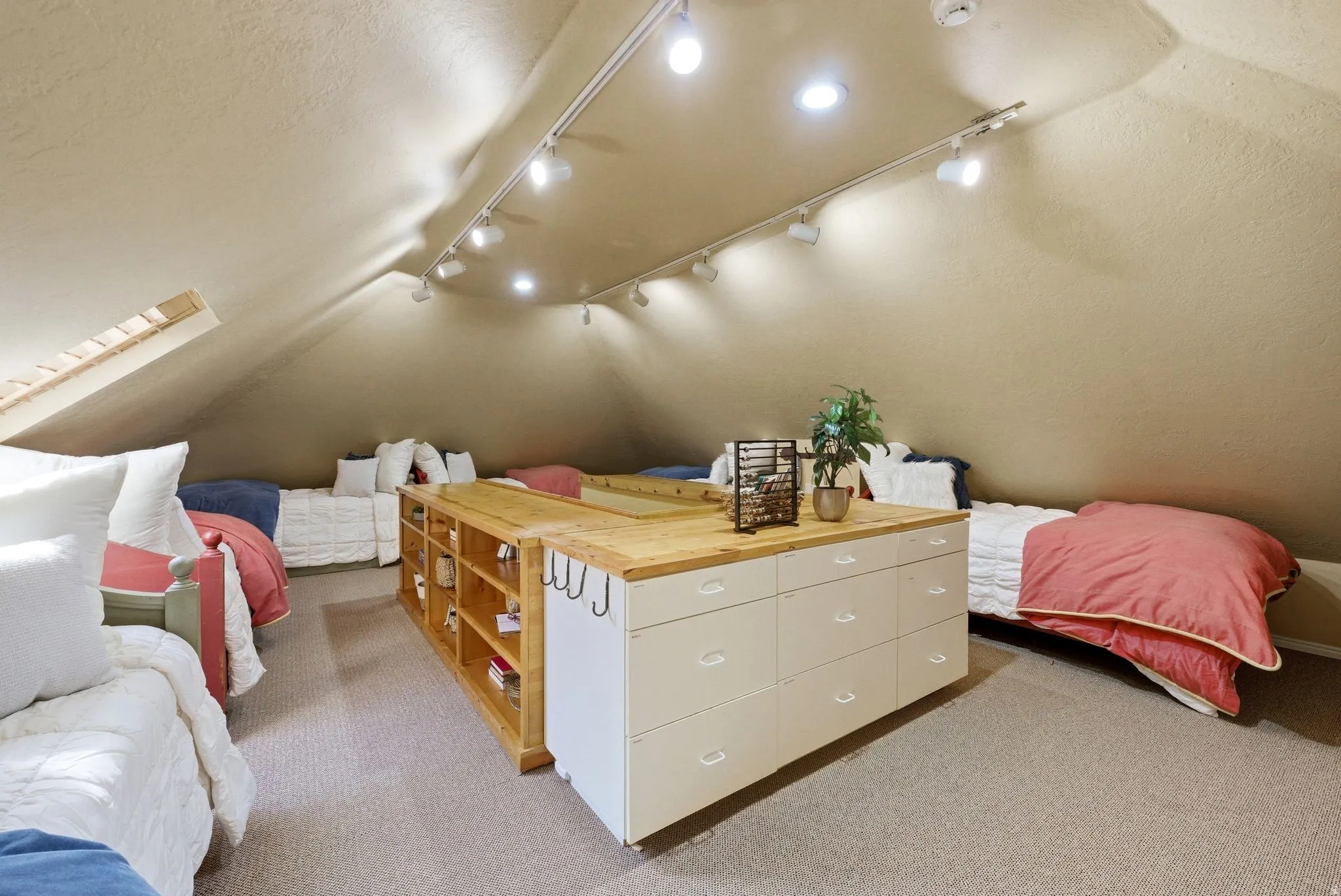 Attic space featuring sloped ceilings, track lighting, light-toned carpeting, and a built-in storage unit with a wood-finish countertop