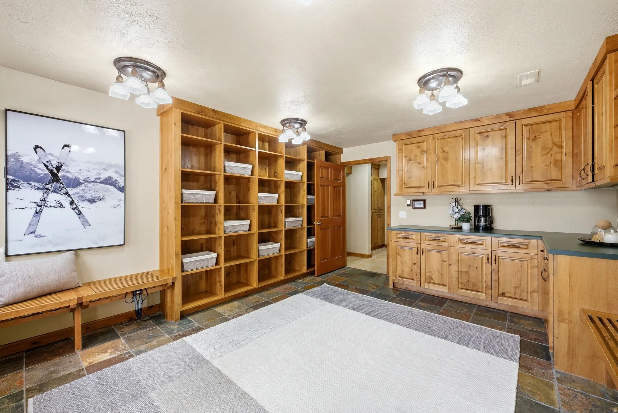 Room featuring extensive custom wood cabinetry and shelving, dark stone tile flooring, and multiple ceiling-mounted light fixtures