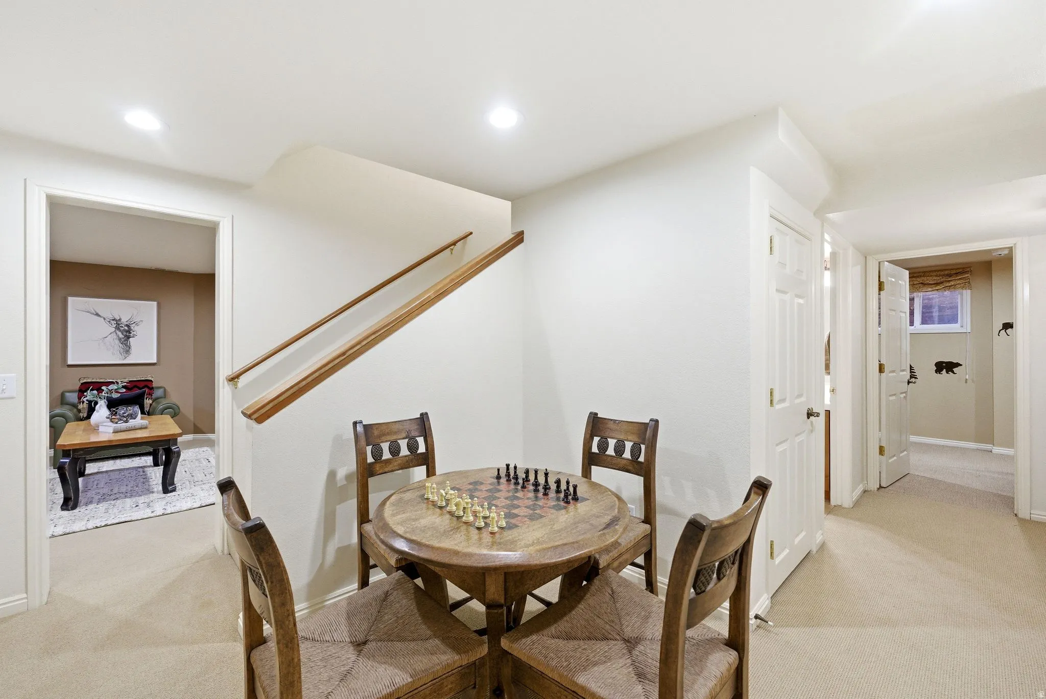 Carpeted lower-level recreation area featuring recessed lighting, a wooden staircase with handrails, and a hallway leading to additional rooms