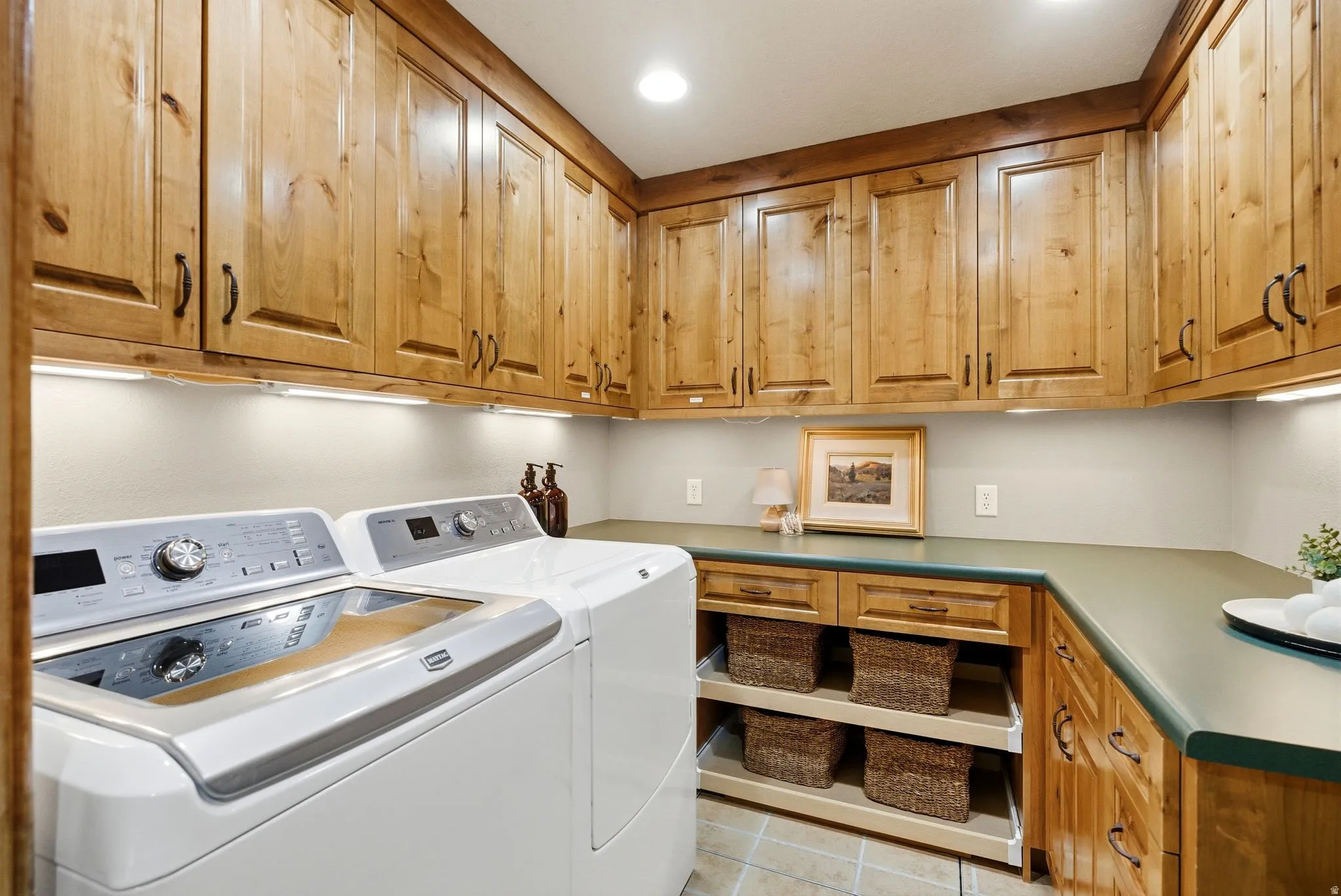 Laundry area featuring extensive wood cabinetry, under-cabinet lighting, a spacious countertop, integrated pull-out storage, and tile flooring