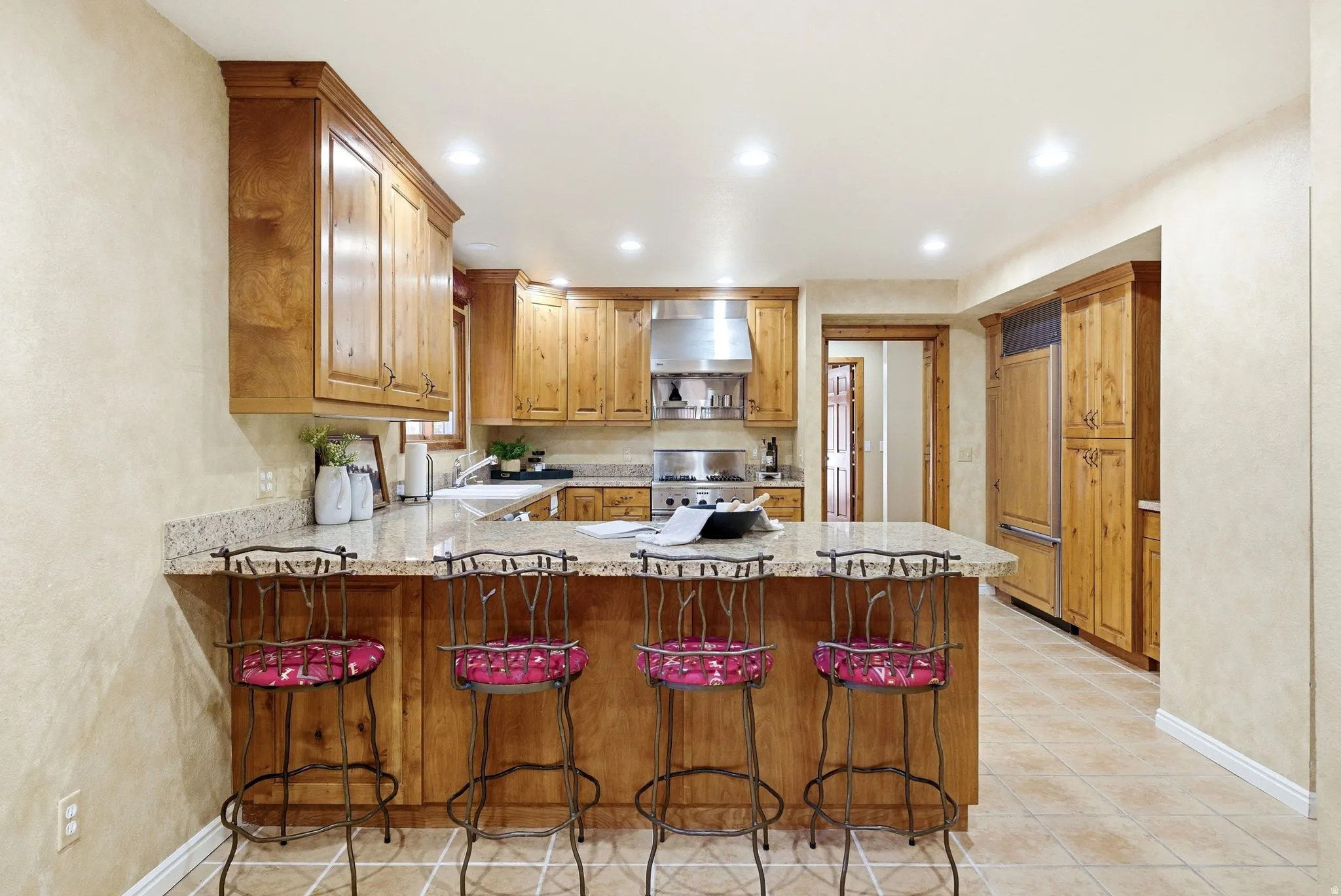 Kitchen featuring a spacious island with a granite-style countertop, abundant wood cabinetry, recessed lighting, stainless steel range hood, and tile flooring