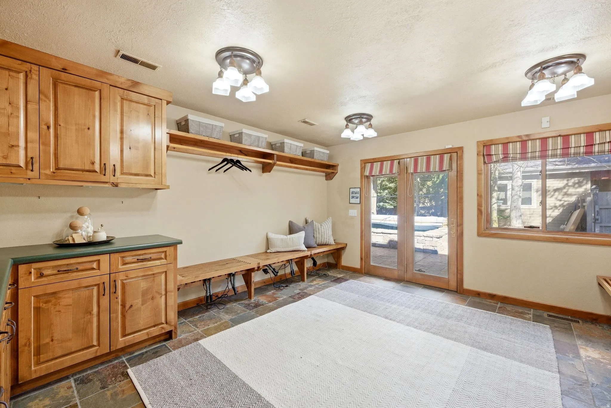 Mudroom featuring natural wood cabinetry, slate tile flooring, built-in wooden benches, and French doors