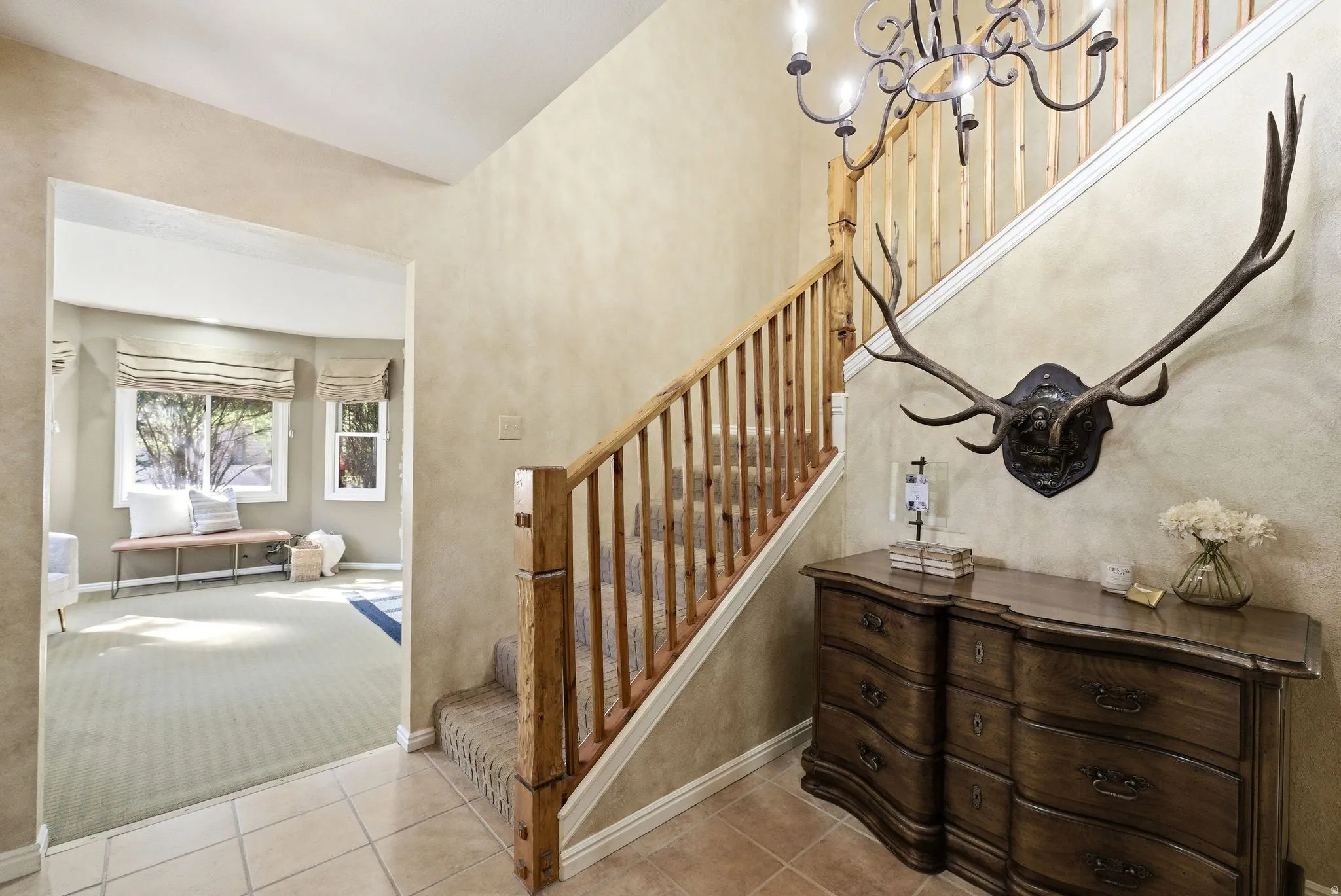 Tiled entryway with a wood staircase featuring a decorative wrought iron chandelier
