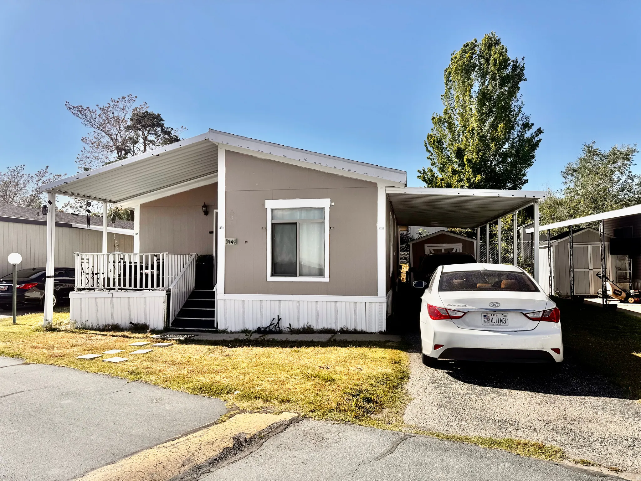 Manufactured home featuring a covered front porch with white railing, covered carport, and exterior storage shed