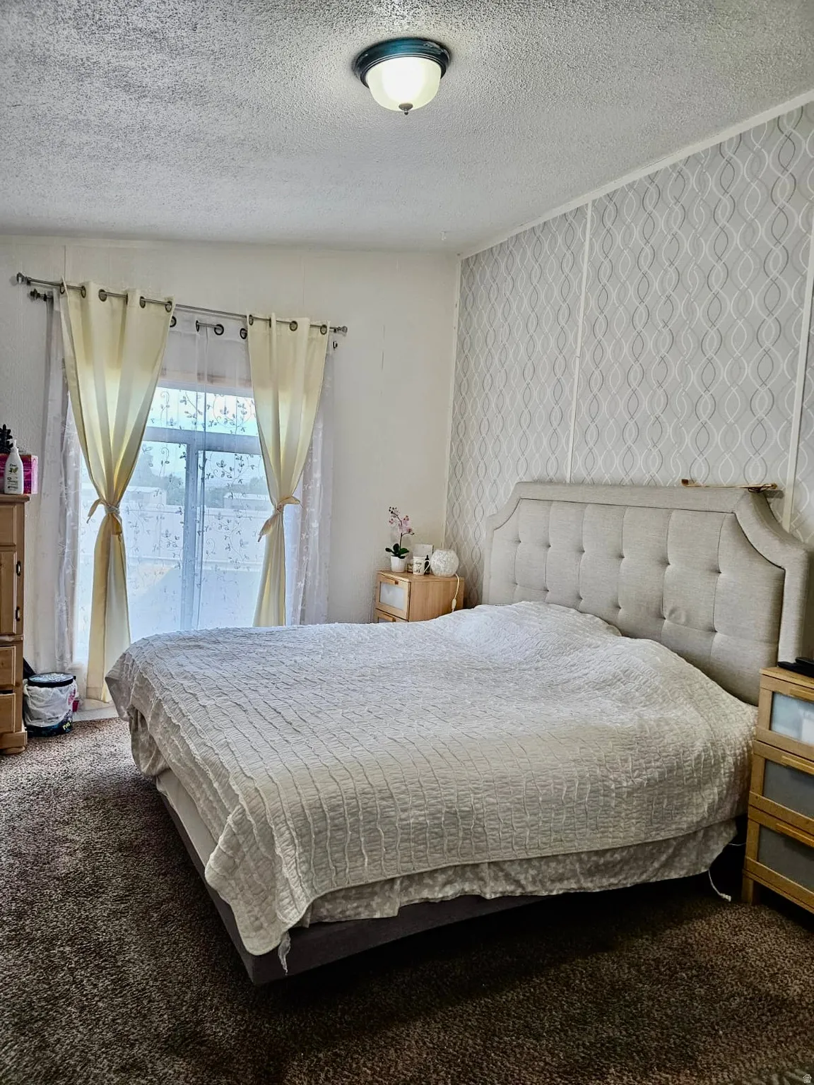 Bedroom featuring textured wallpaper accent wall and a window with sheer and solid curtains
