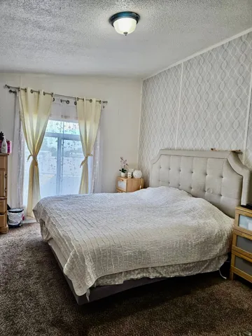 Bedroom featuring textured wallpaper accent wall and a window with sheer and solid curtains